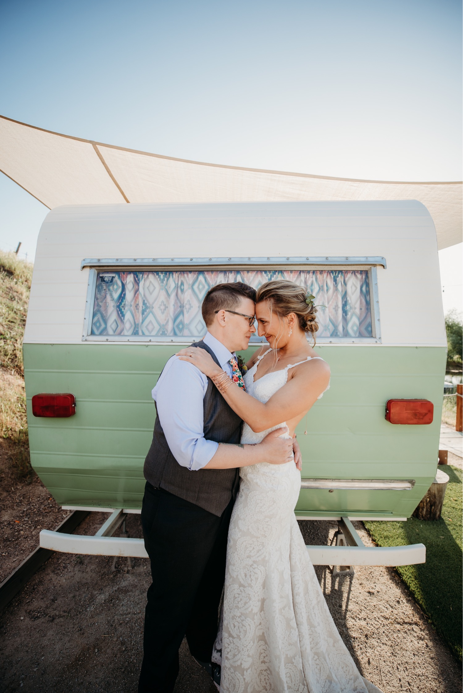 Brides embrace touching foreheads touching foreheads in front of a green and white trailer at their Paso Robles vineyard wedding reception. Liz Koston Photography.