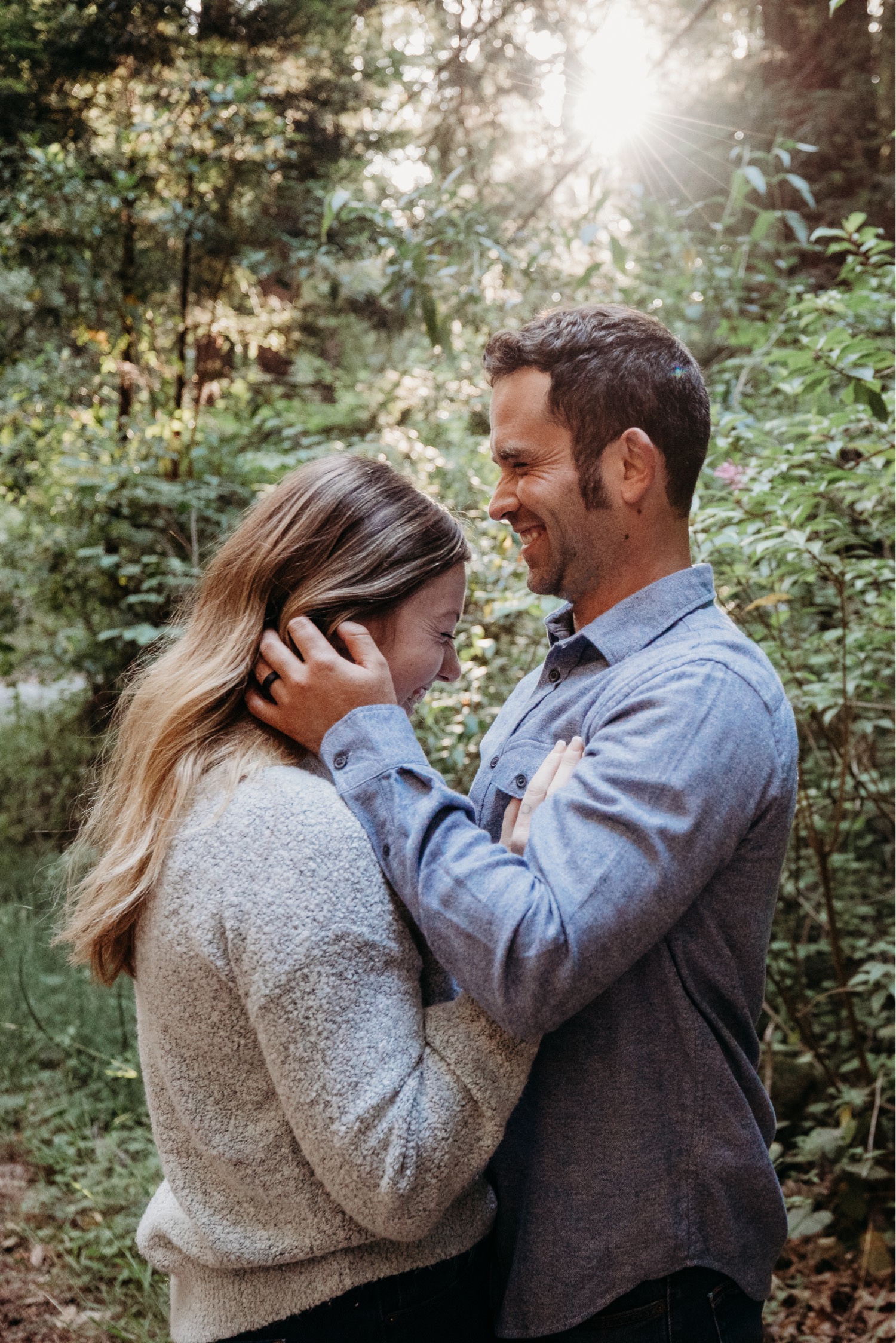 Couple laugh with each other as the man brushes his fiance's hair out of her face during their Big Sur engagement photoshoot.