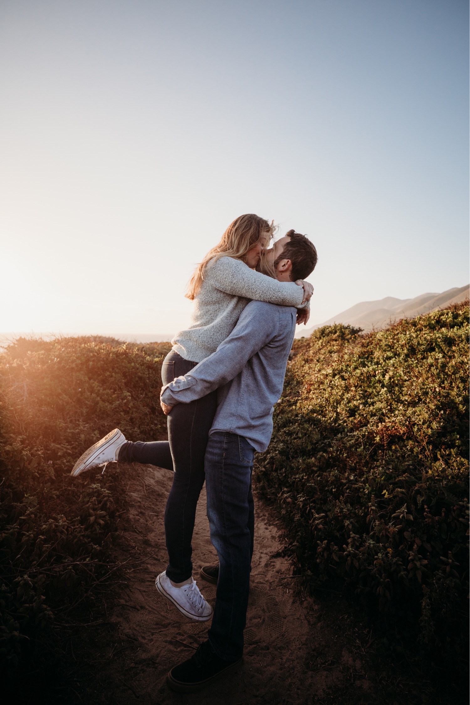 Man lifts woman as they kiss passionately at sunset during their engagement photoshoot in Big Sur, California.