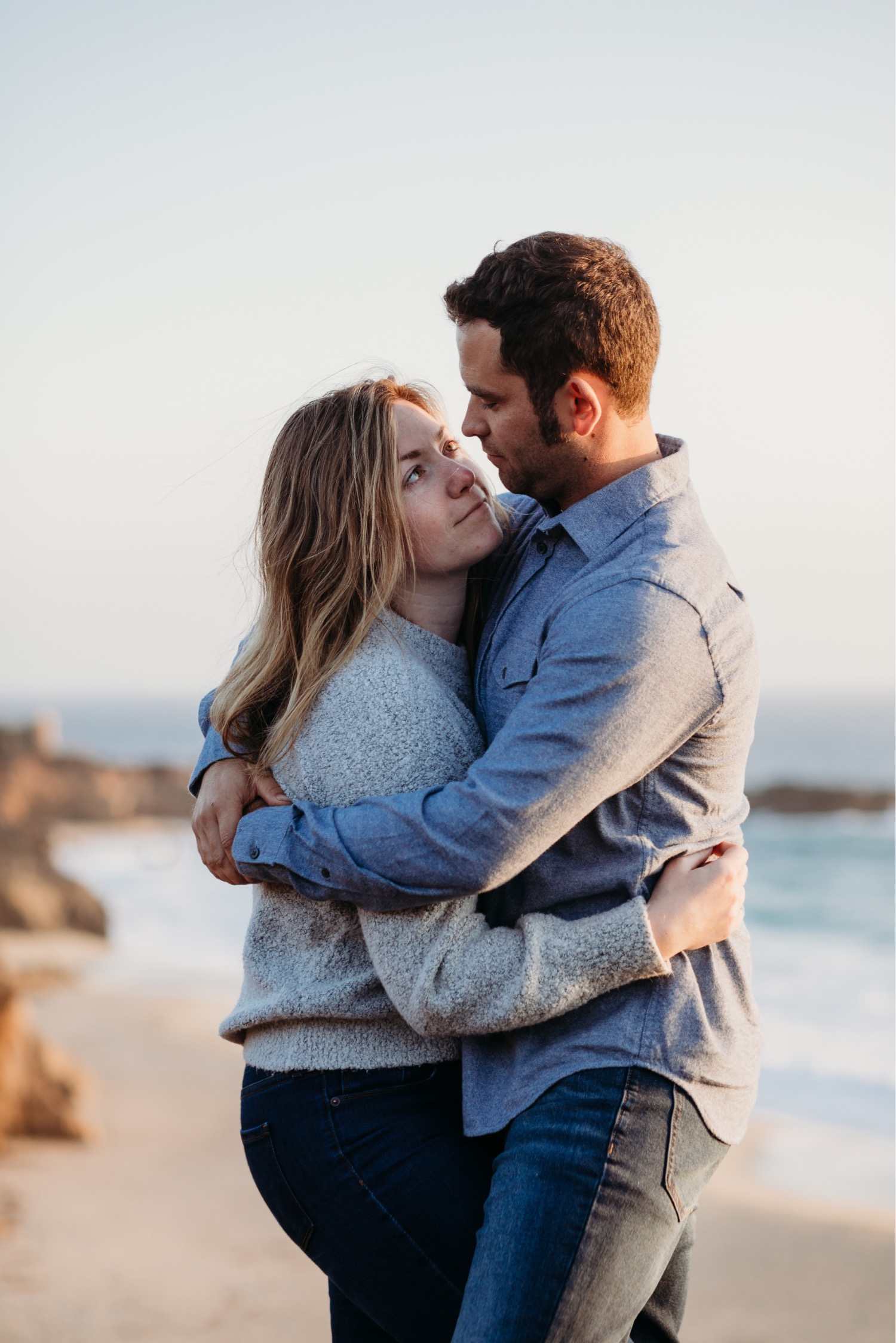 Couple embraces and gaze lovingly at each other with the beach in Big Sur in the background on their Big Sur engagement photoshoot.