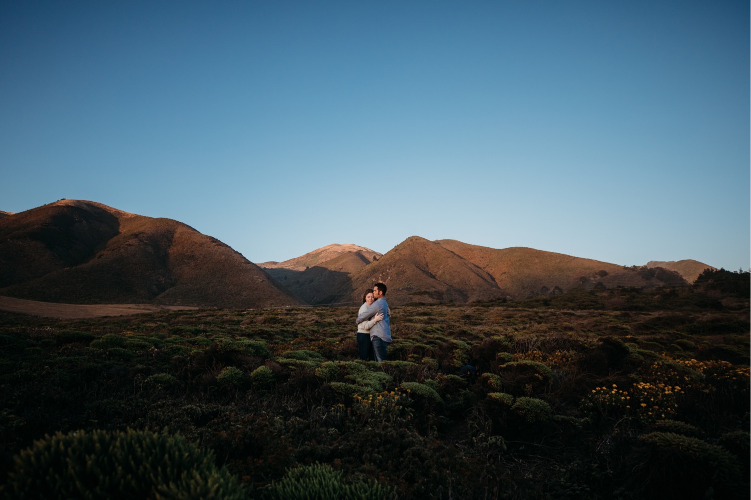 Couple embrace surrounded by the mountains of Big Sur, California during their engagement photoshoot.