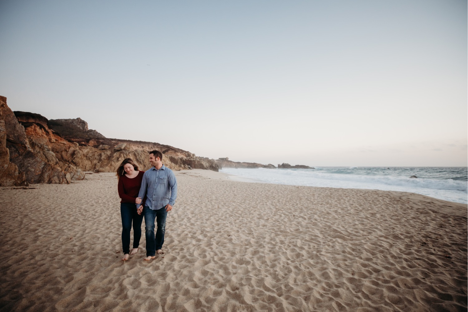 Couple walks hand in hand along the beach at sunset on their Big Sur, California engagement photoshoot.