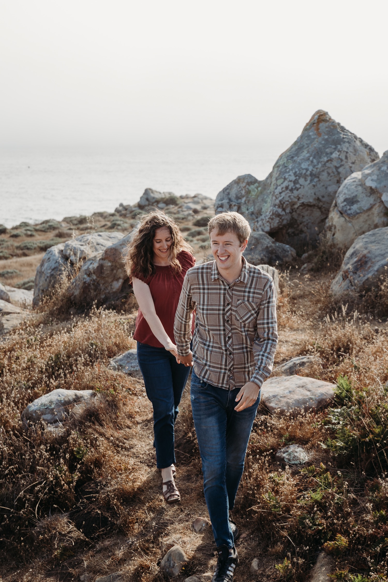 Man leads his fiance by the hand while walking on a trail in Salt Point State park during their engagement session.