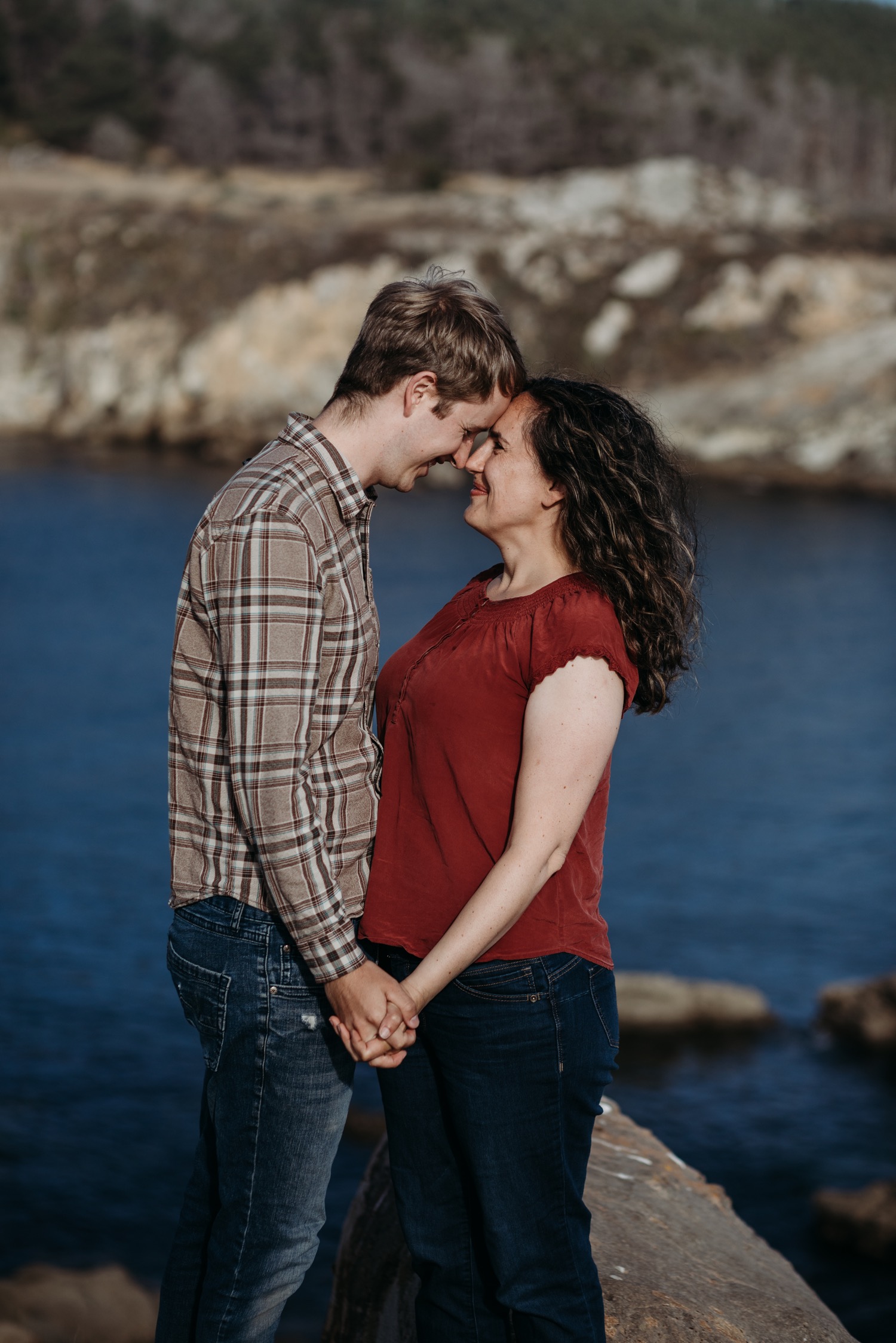 Couple during their Salt Point Park engagement photoshoot stands facing each other holding hands and foreheads touching with big smiles. 