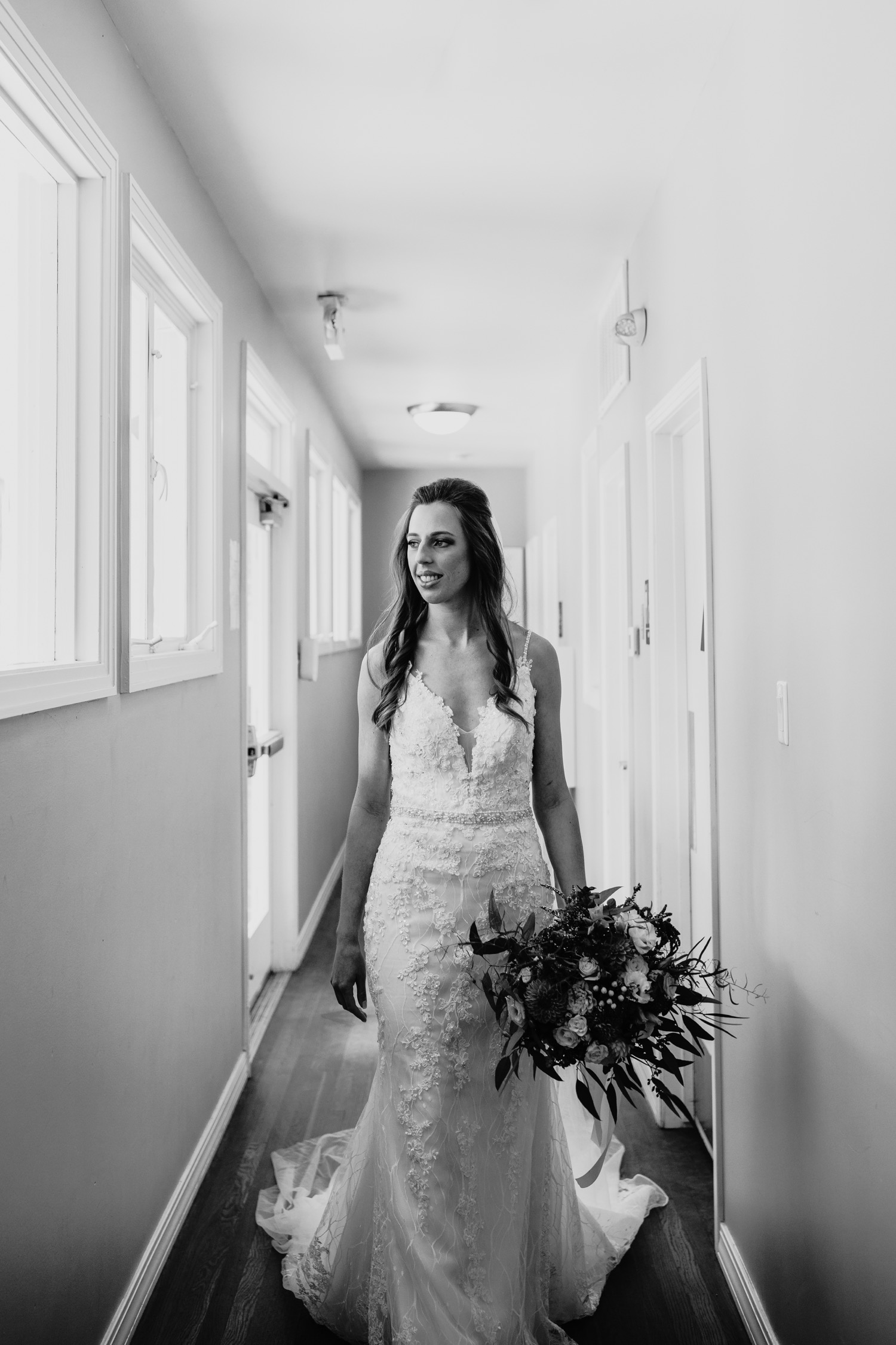 Black and white image of the bride walking down a hallway at The Maples holding her bouquet.