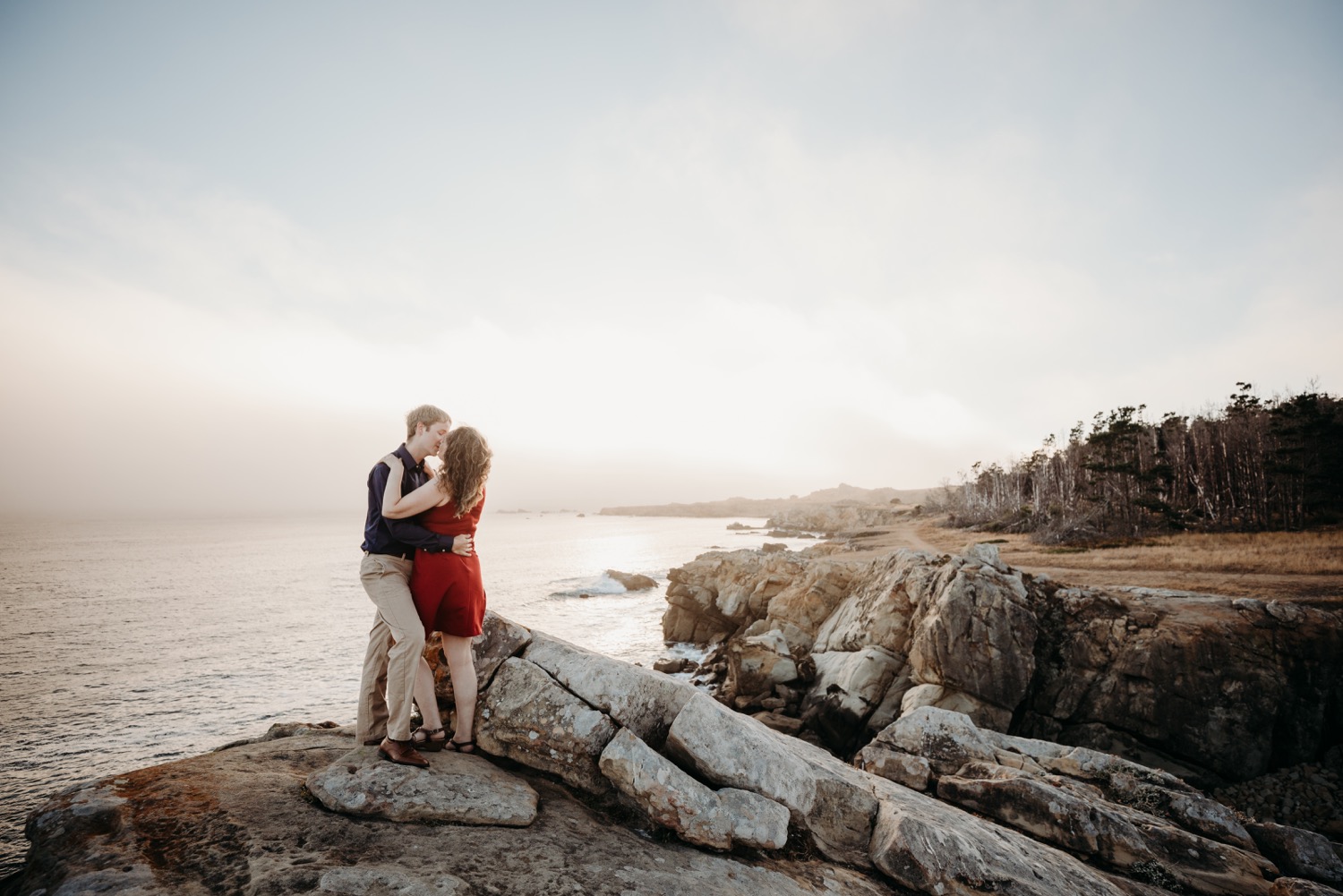 Couple kisses at sunset overlooking the Pacific Ocean during their couple engagement session in Salt Point Park.
