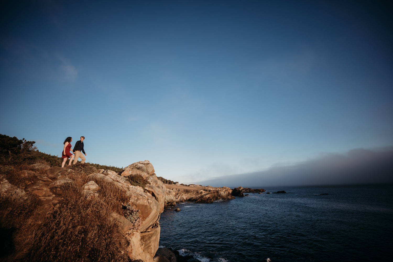 Couple walks on a bluff overlooking the Pacific Ocean during their engagement photoshoot in Salt Point State Park