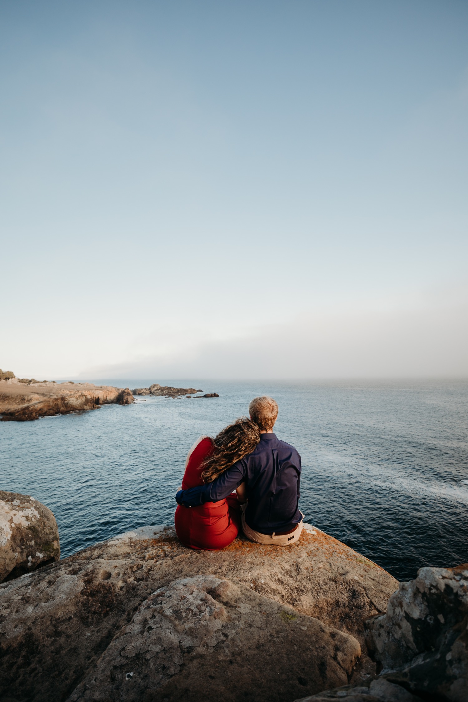 Couple sits together on a rock over looking the Pacific Ocean during their Salt Point State Park Engagement Photoshoot