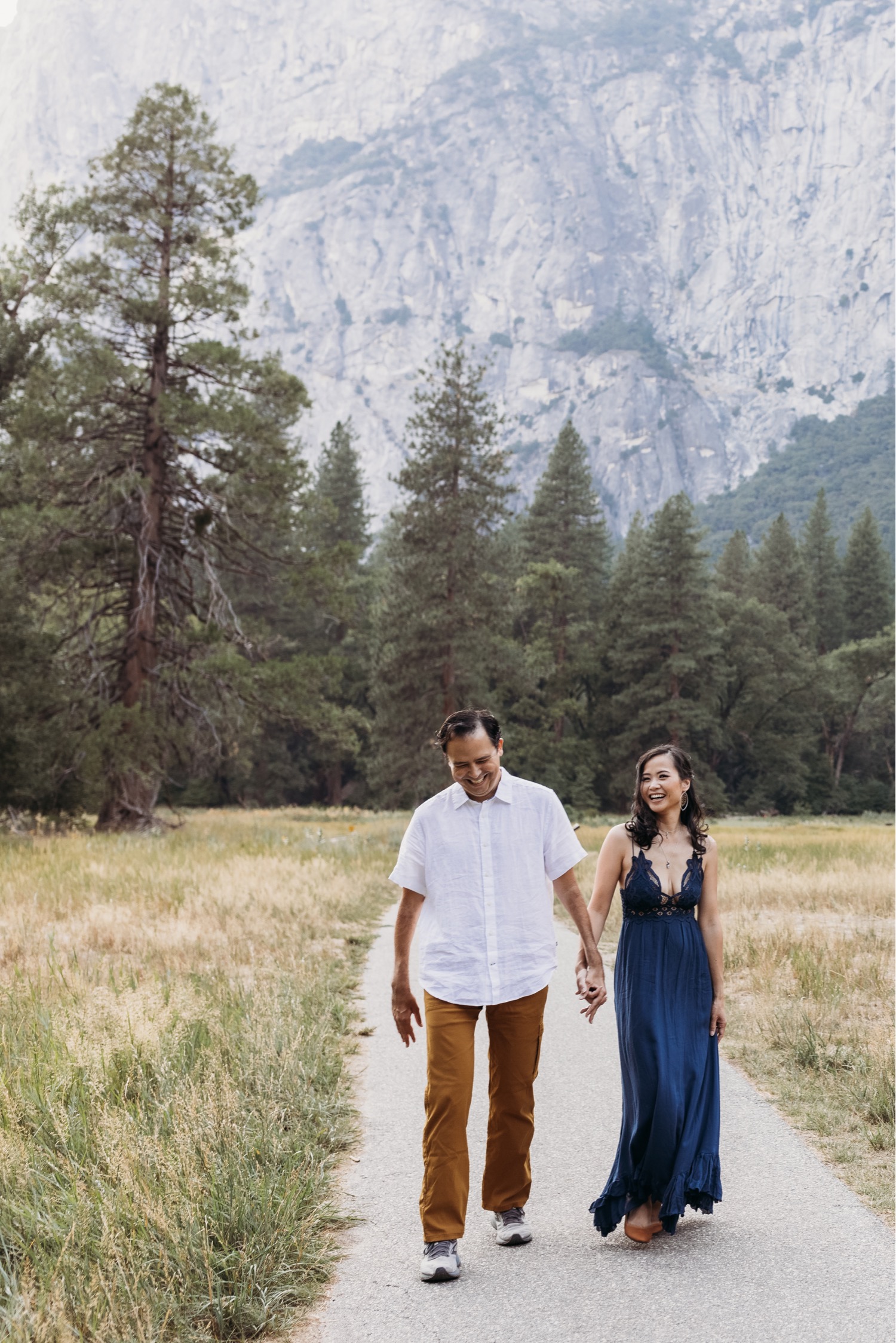 Couple walks smiling down a path in Yosemite Valley during their Yosemite couples photoshoot