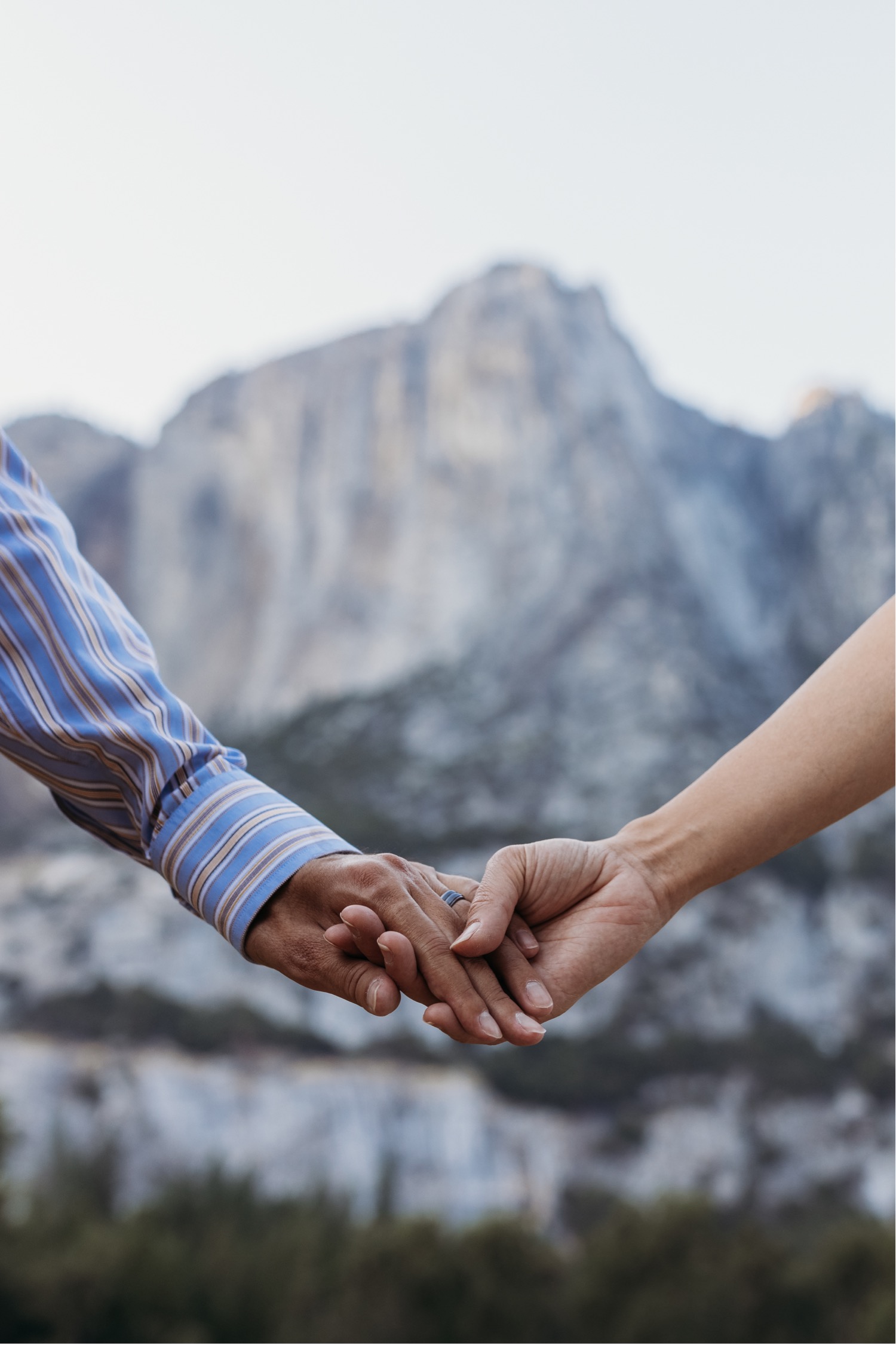 Up close image of two hands holding with a view of Yosemite in the distance taken by Yosemite photographer Liz Koston.