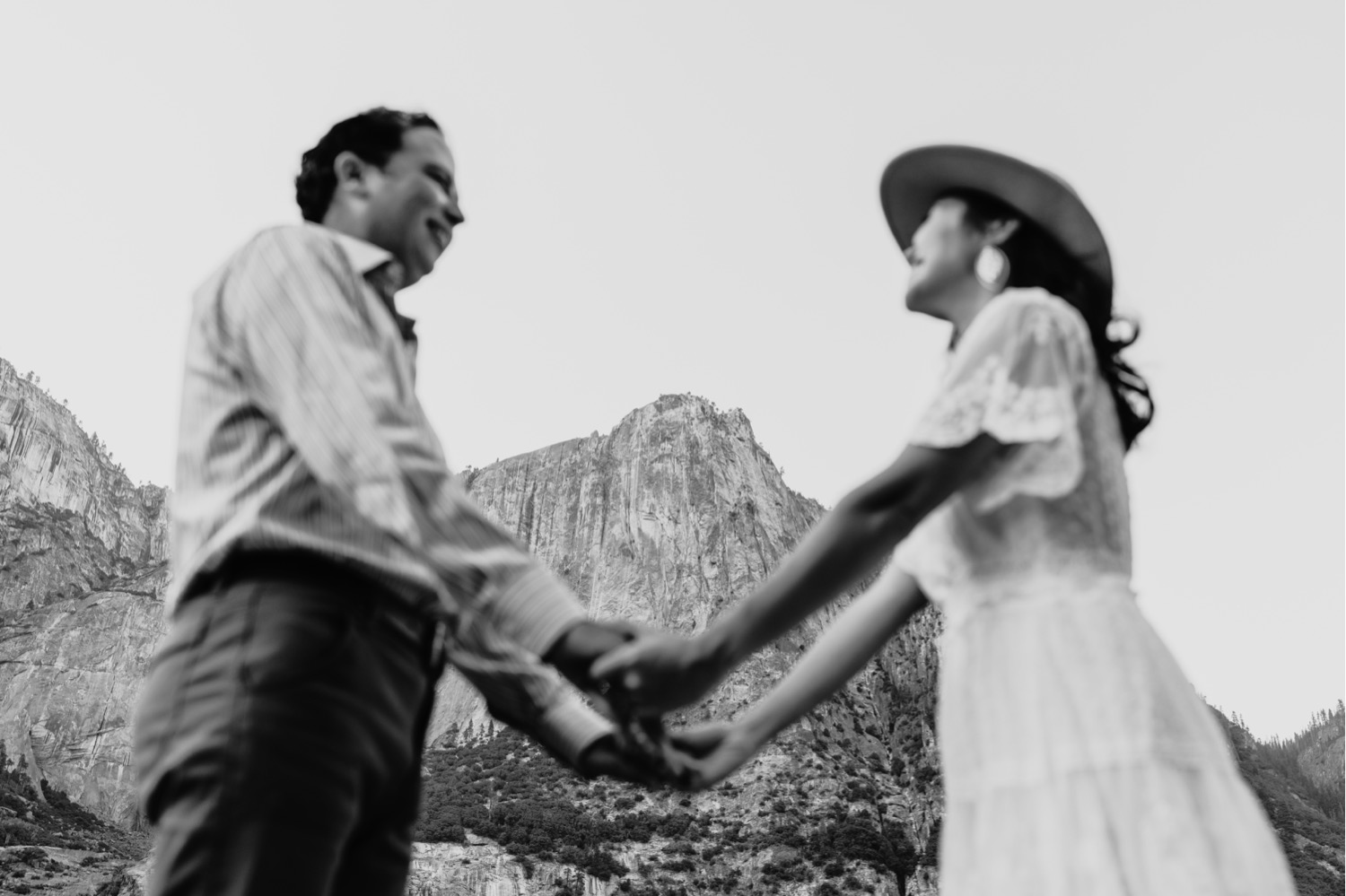 black and white image of couple smiling and holding hands with Yosemite in the background