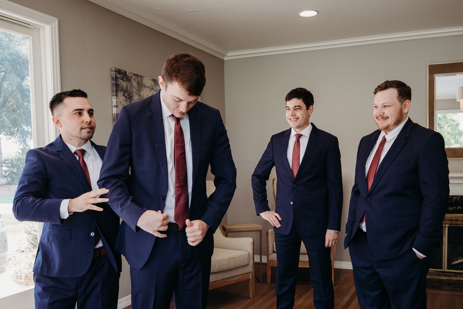 Groomsmen helps groom into his jacket while other groomsmen look on. Alayna and Trey's wedding at The Maples in Woodland, CA. 