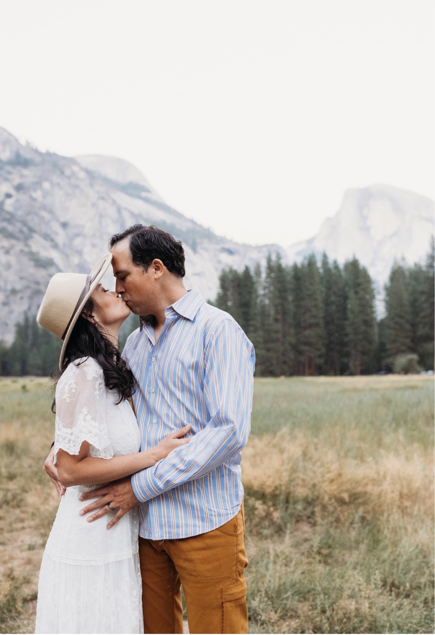 Couple kisses while in an embrace with Yosemite National Park in the distance.