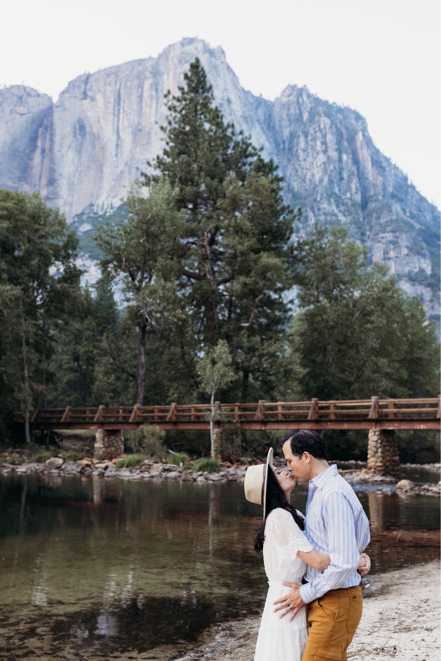 Couple kisses near a small lake underneath the tall Yosemite peaks. Photo taken by Yosemite photographer Liz Koston.