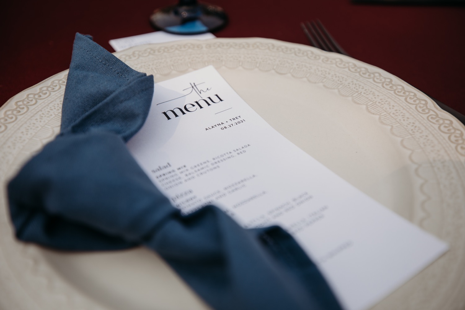 Dinner menu on plate with a blue napkin for Alayna and Trey's wedding at The Maples in Woodland, CA