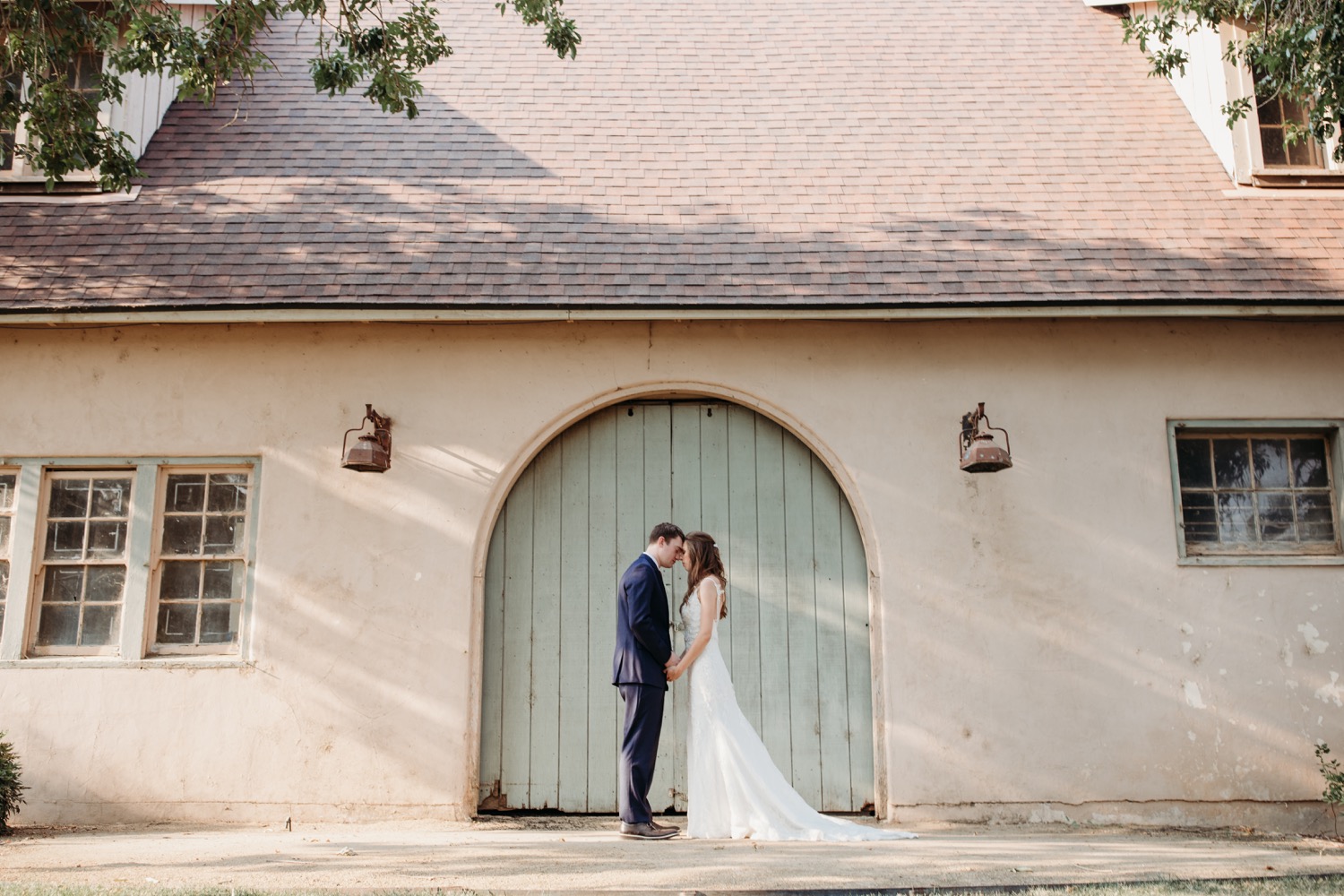 Bride and groom stand with foreheads touching in front of a green door at The Maples in Woodland, CA
