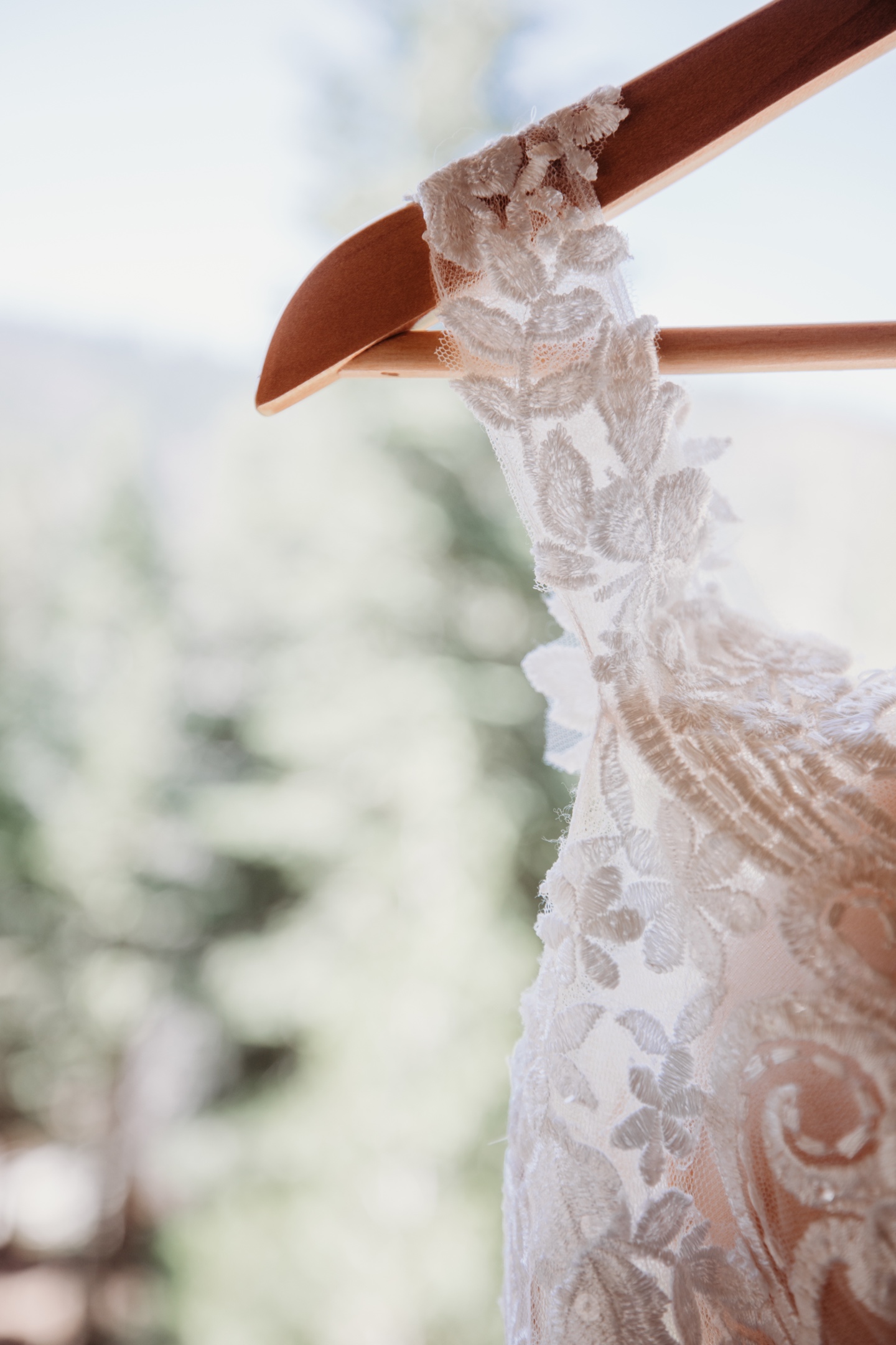 Lace shoulder of wedding dress hands on wooden hanger with Yosemite forest in background