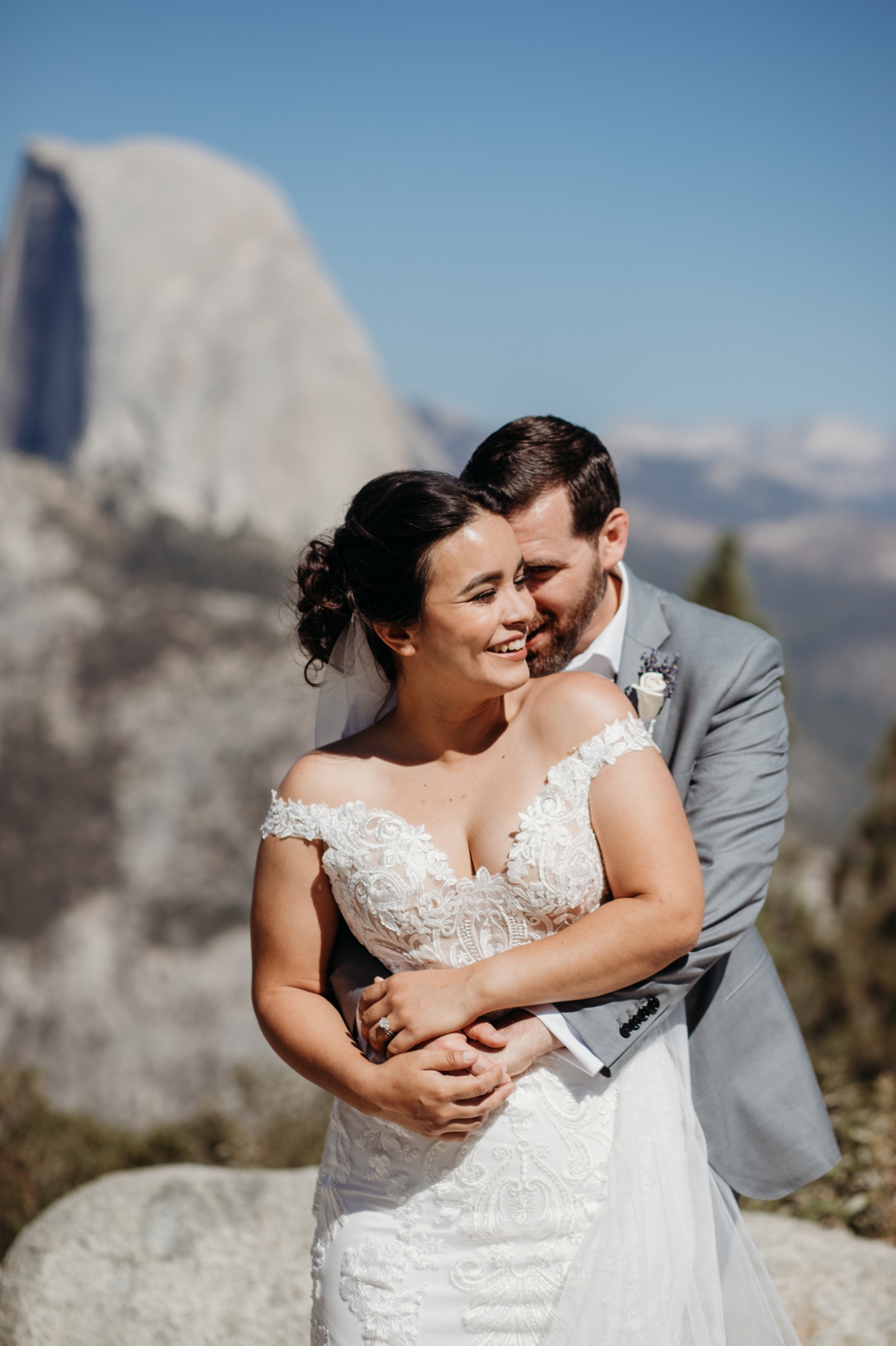 Groom hugs bride from behind while they smile widely after their Yosemite elopement.