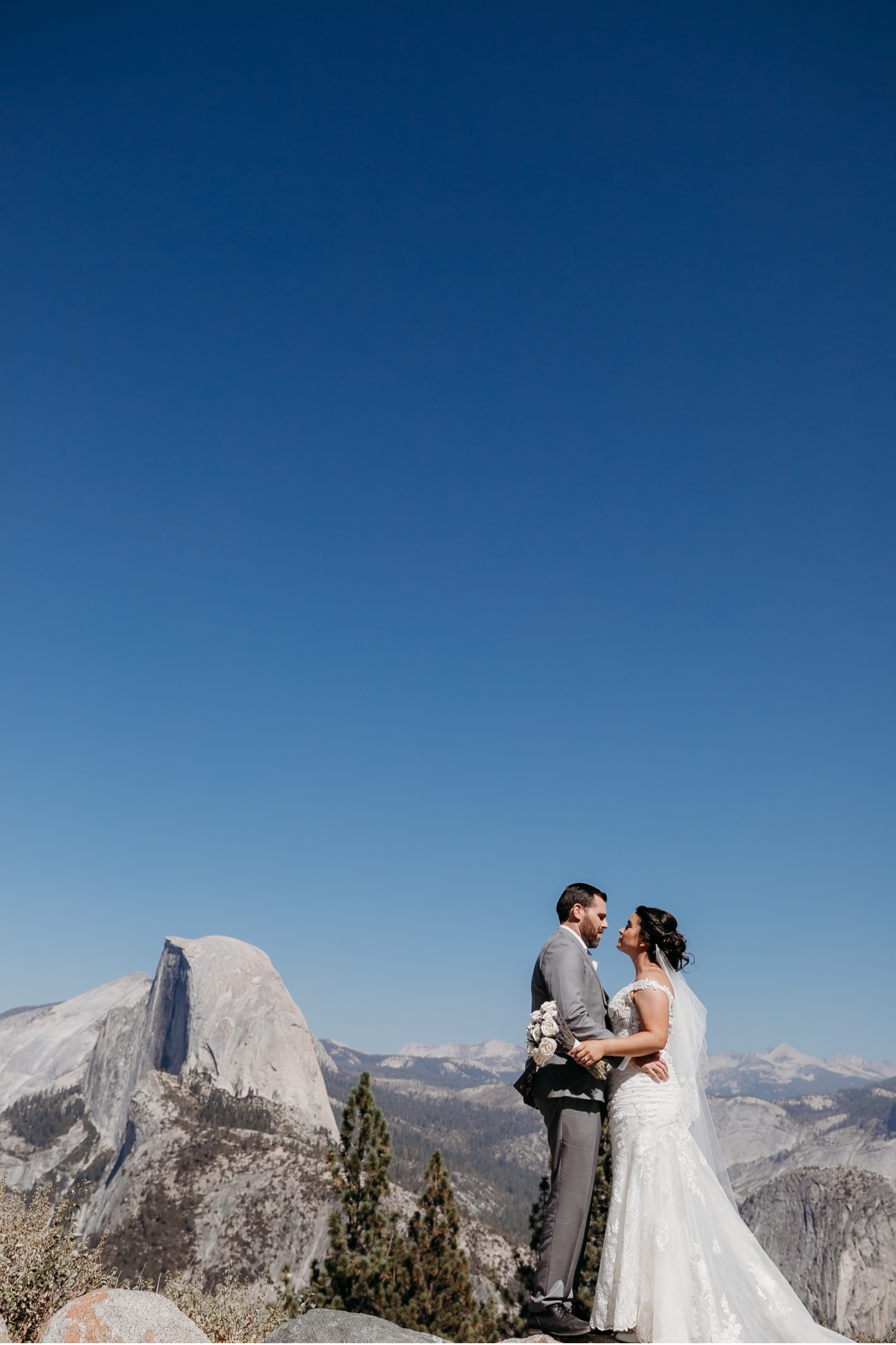 Bride and groom hold each other while gazing in each other's eyes with Half Dome in the distance. 