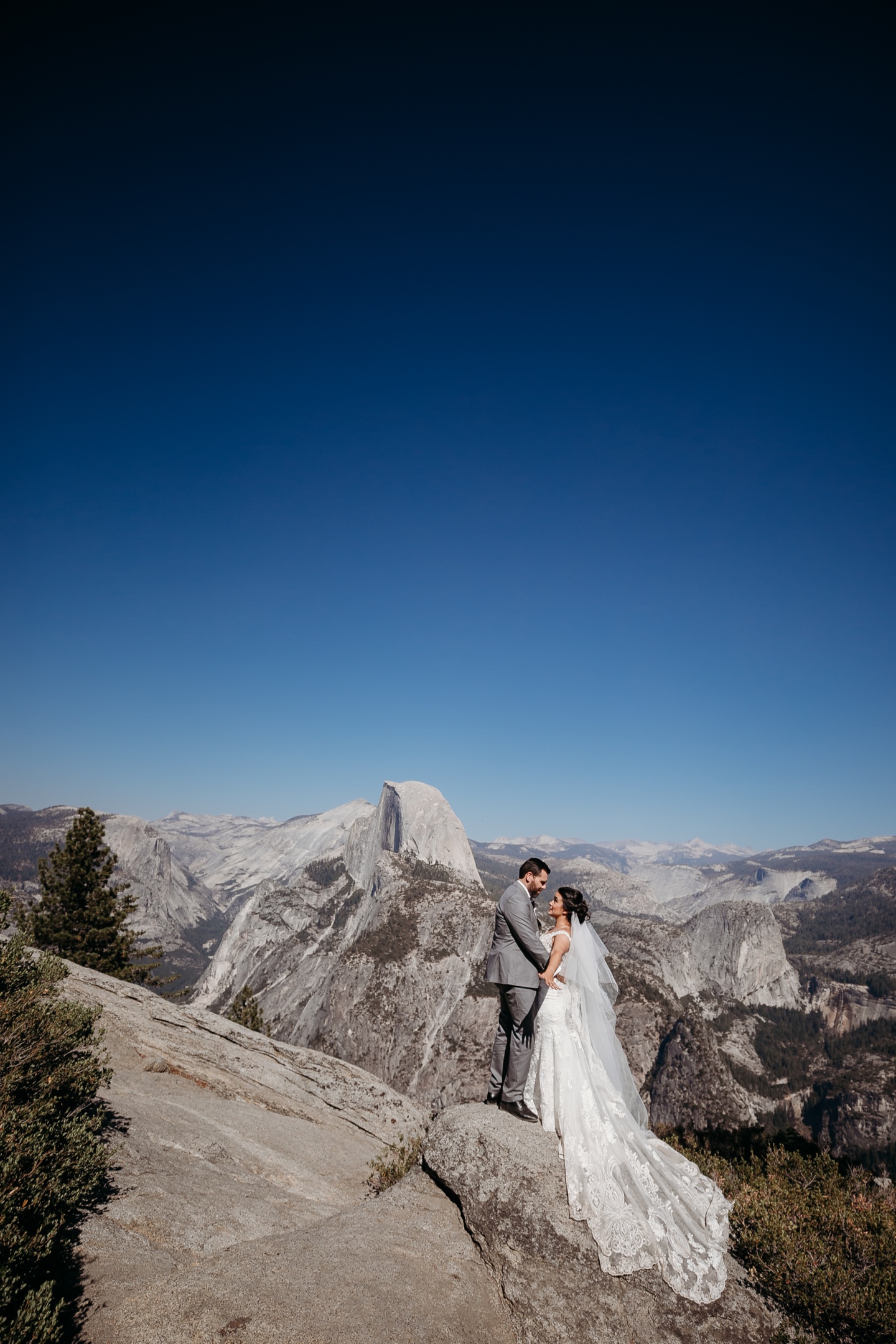 Dramatic image of bride and groom embracing each other with Half Dome and Yosemite National Park in the background.