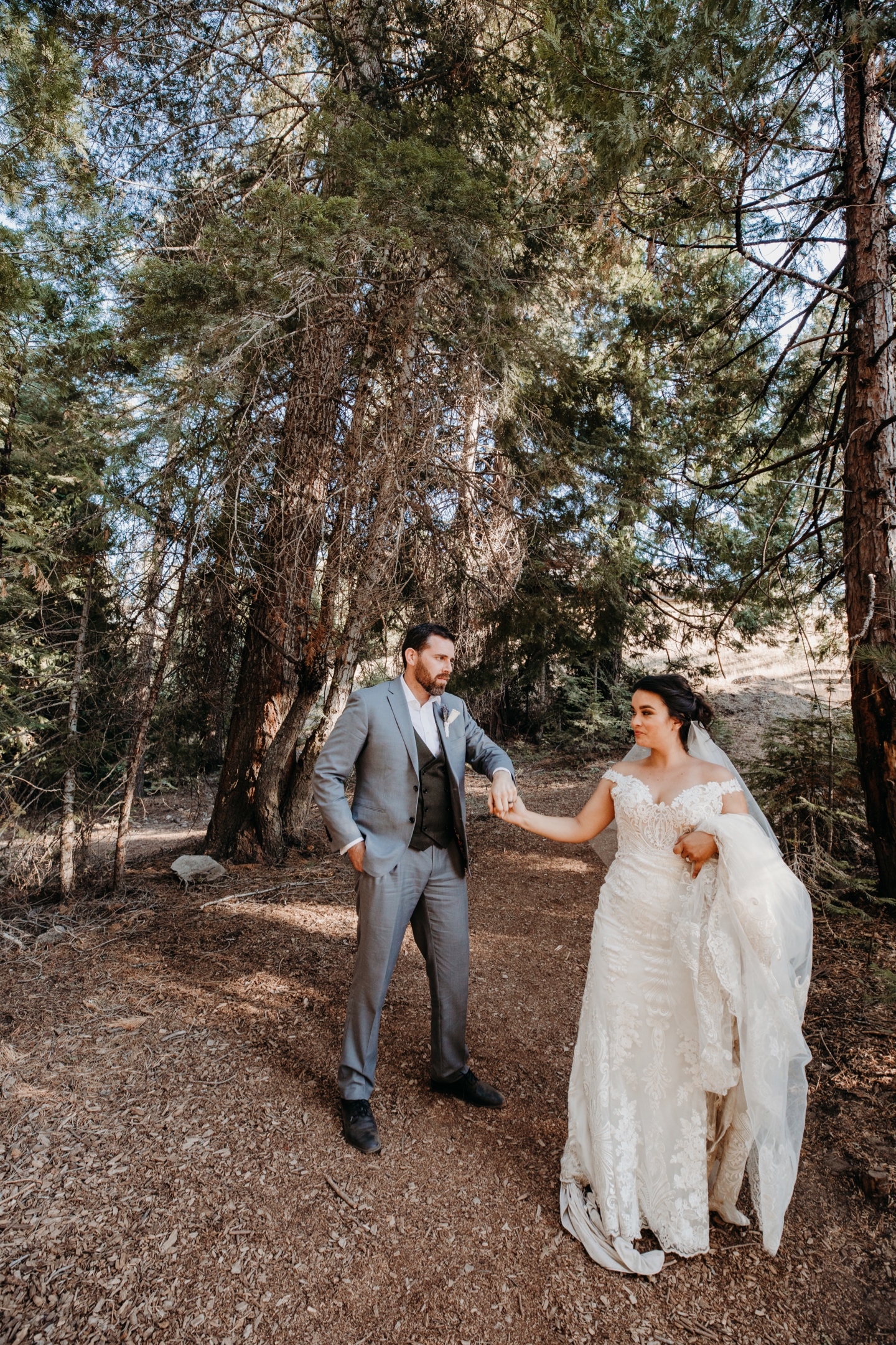 Bride leads groom by the hand down a trail in Yosemite surrounded by Pine trees.