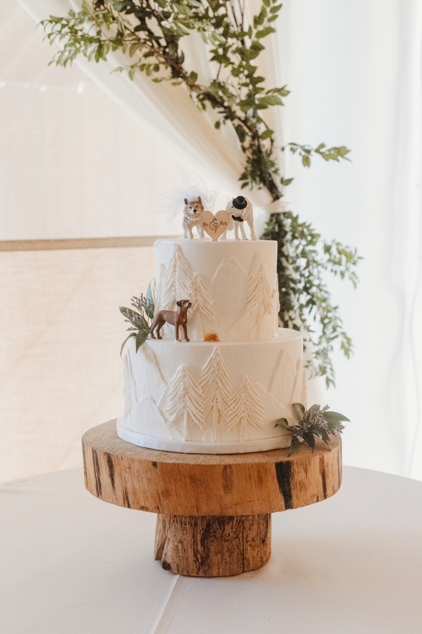 Two tier wedding cake decorated with trees and dog figurines on wood cake stand. Wedding cake is perfect for a Yosemite wedding.