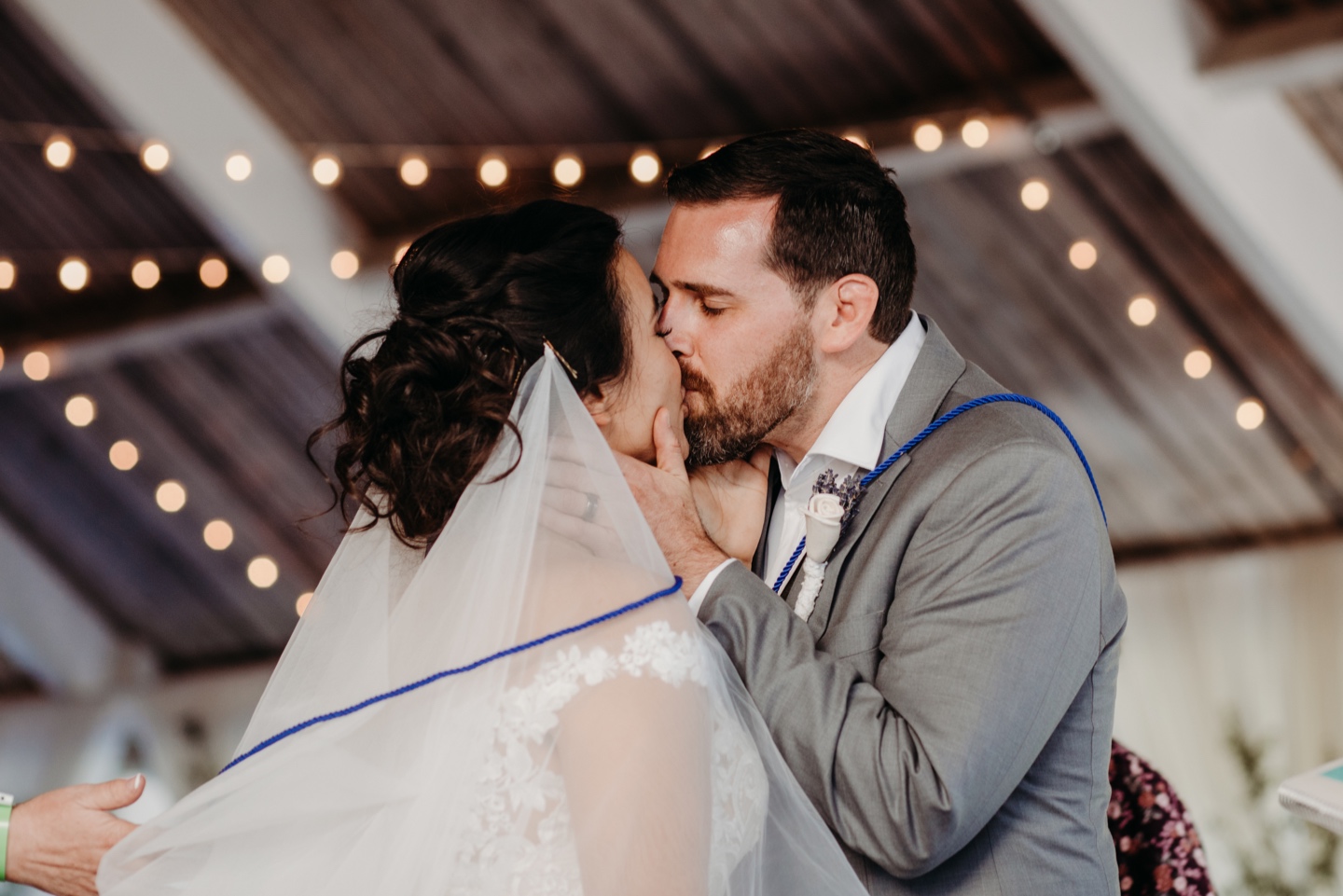 Bride and groom kiss with blue yarn wrapped around their shoulders