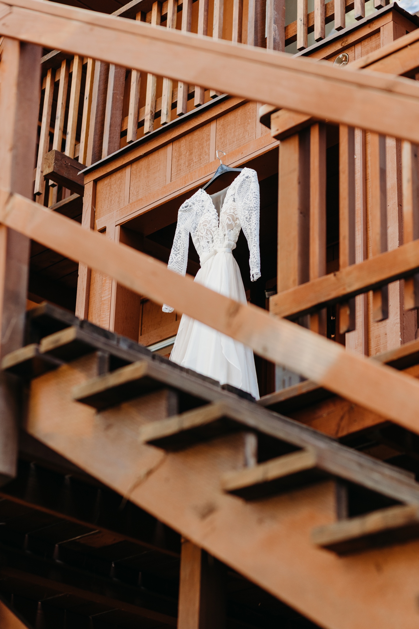 Wedding dress hangs from wood a deck as seen from the bottom of the stairs. 