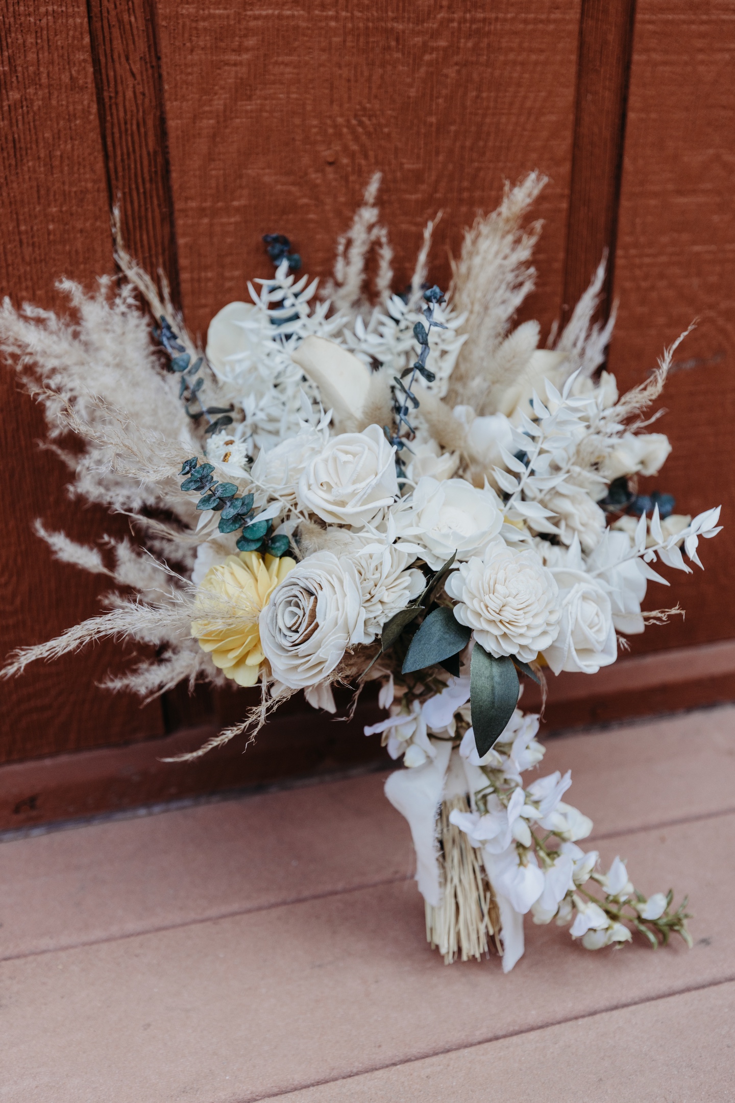 Bouquet of white, yellow, and sage flowers lean up against a Yosemite cabin wall. 