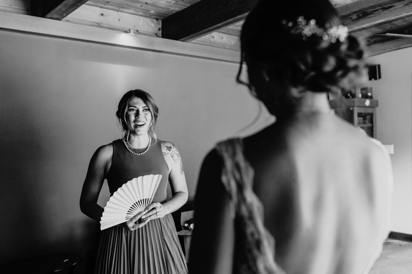 Bridesmaid smiles wide at the bride while holding a fan. Sacramento wedding photography by Liz Koston.