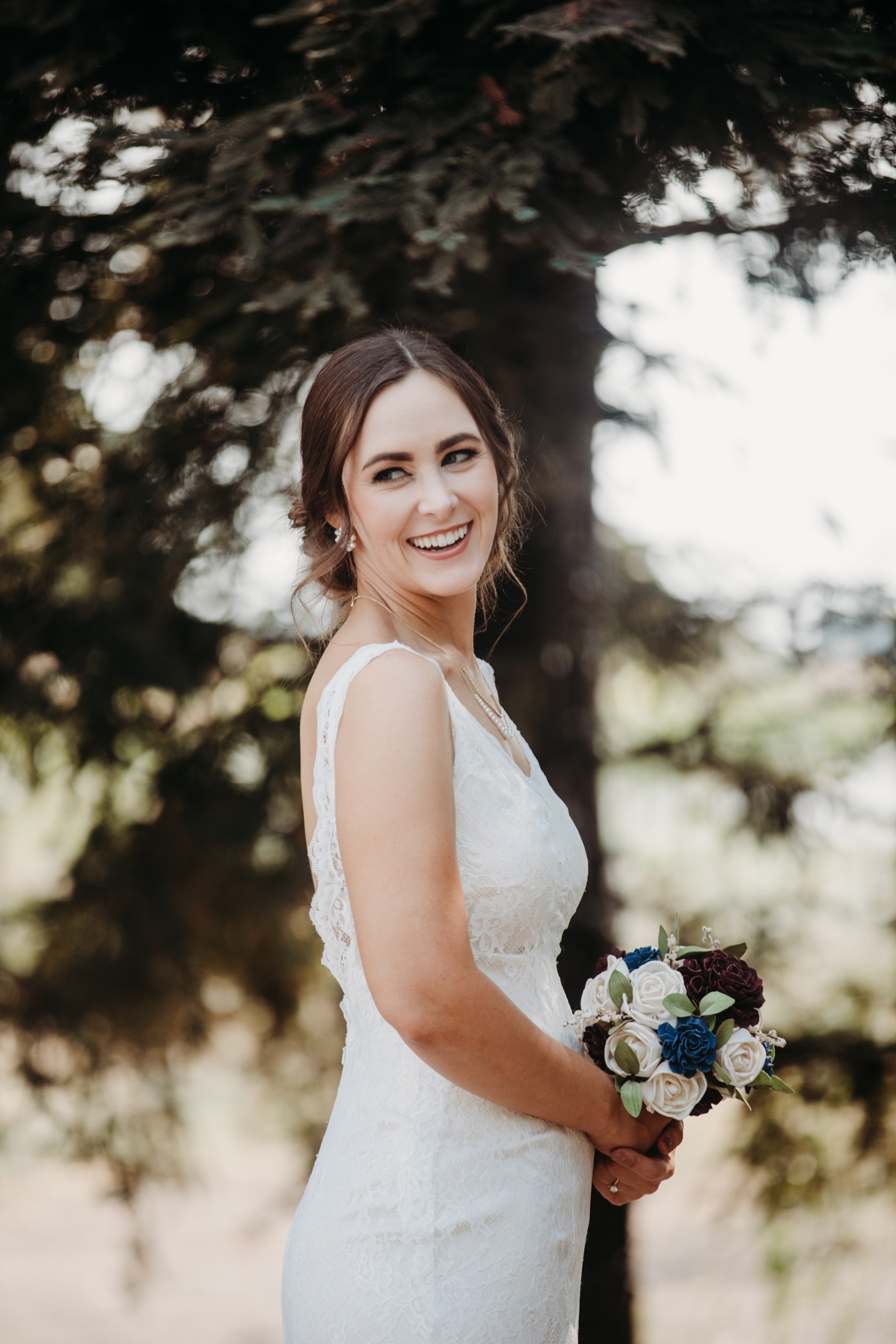 Bride in her wedding dress holds her bouquet of flowers as she smiles and looks over her shoulder. Sacramento wedding photography by Liz Koston.
