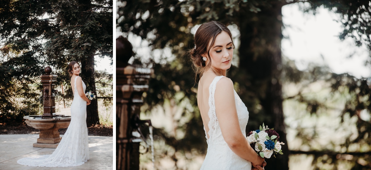 Bride stands in front of a fountain in her white lace wedding dress and looks over her shoulder while holding her flower bouquet. Beautiful wedding photography in Sacramento by Liz Koston.