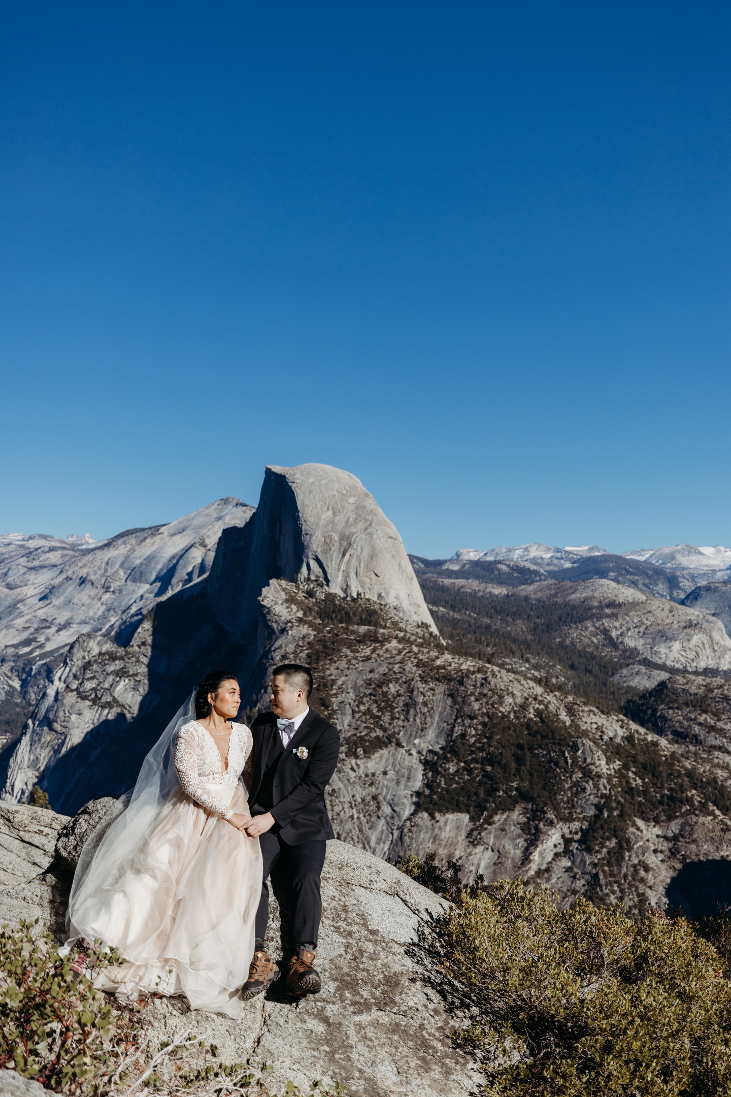 Bride and groom sit side by side looking into each other's eyes with Half Dome in Yosemite as their background. 