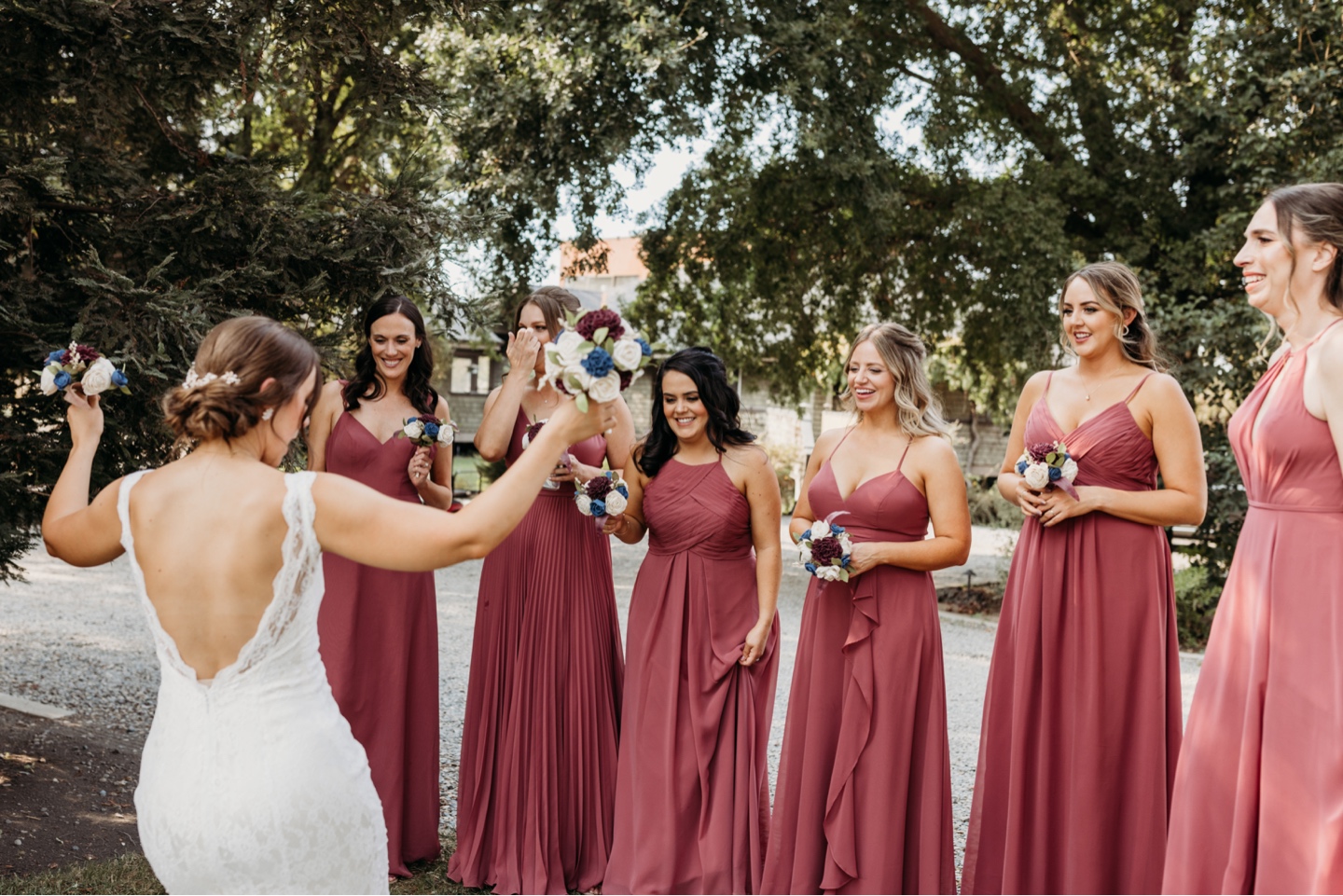 Bride shows off her wedding dress to her bridesmaids all wearing dark pink bridesmaids dresses. Wedding photography in Sacramento by Liz Koston.