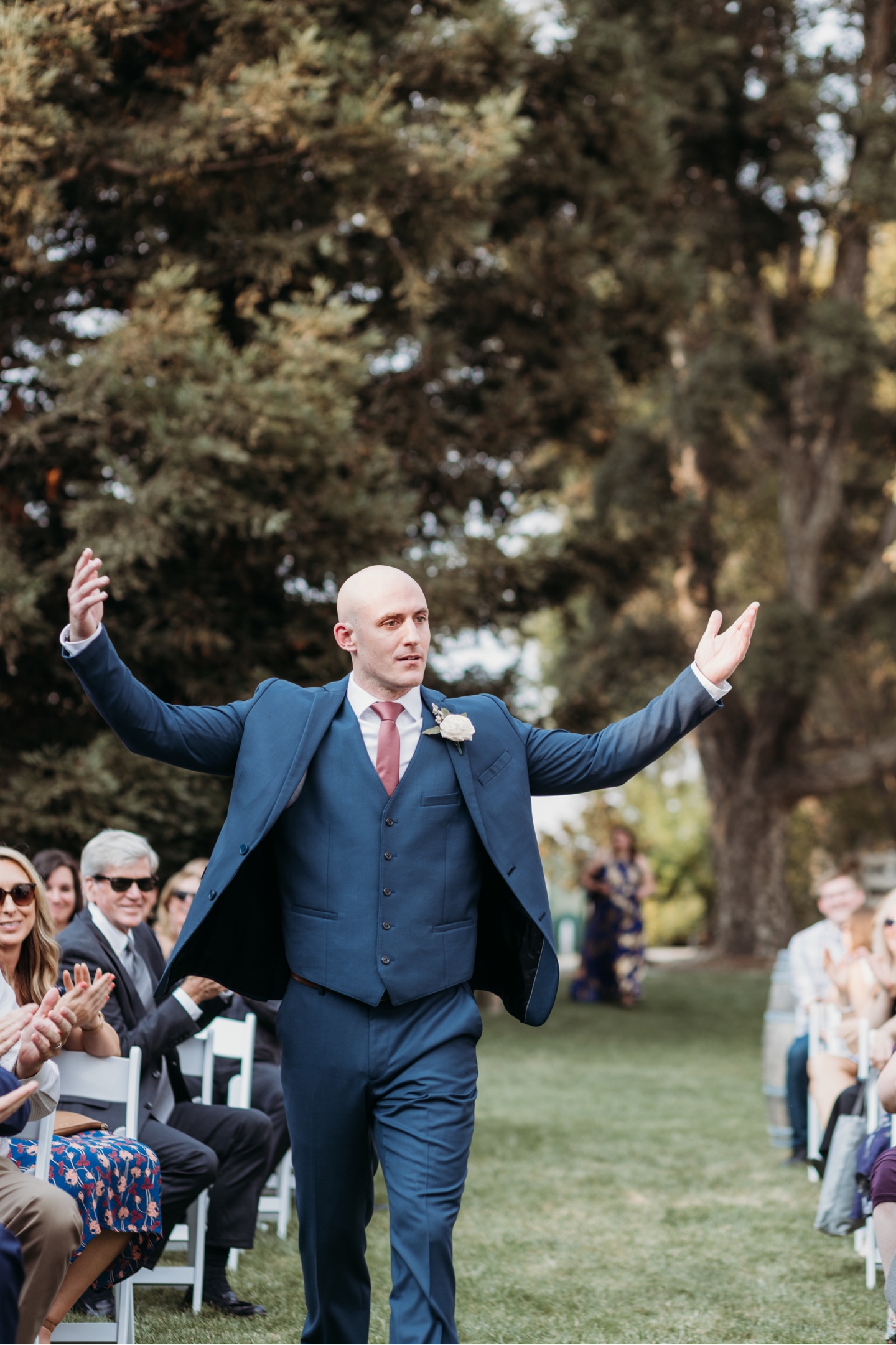 Groom walks down the aisle raising his arms overhead. Sacramento wedding photography by Liz Koston.