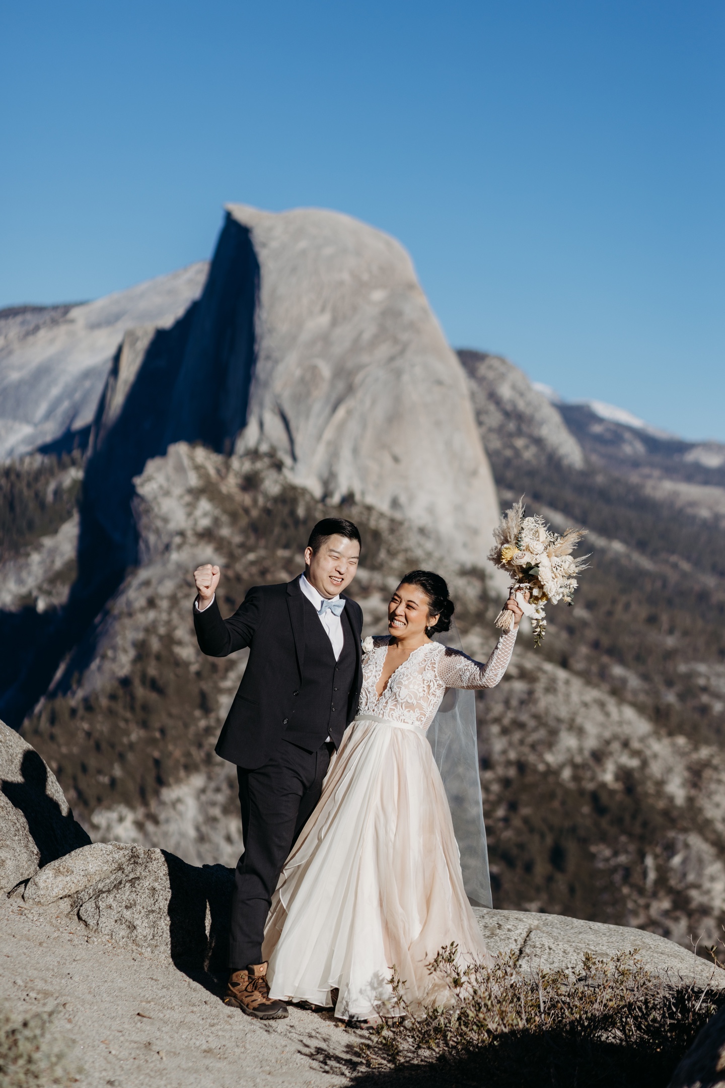 Bride and groom fist pump in celebration of their Yosemite elopement with Half Dome in the distance.