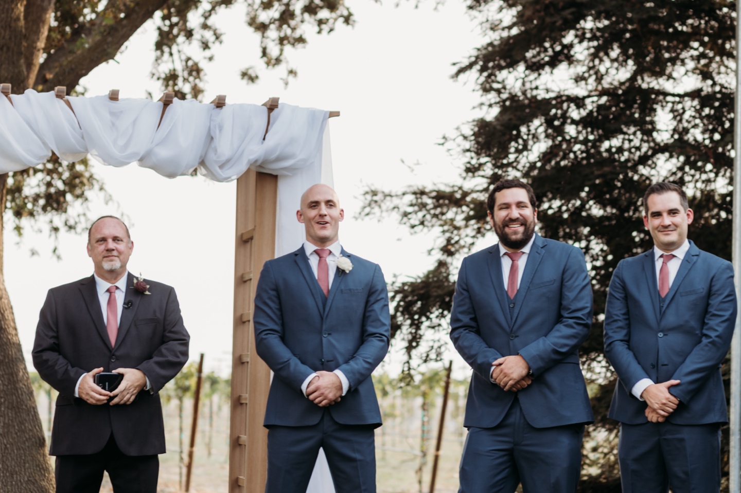 Groom and groomsmen stand at the altar with the officiant and smile big! Wedding photography in Sacramento by Liz Koston.