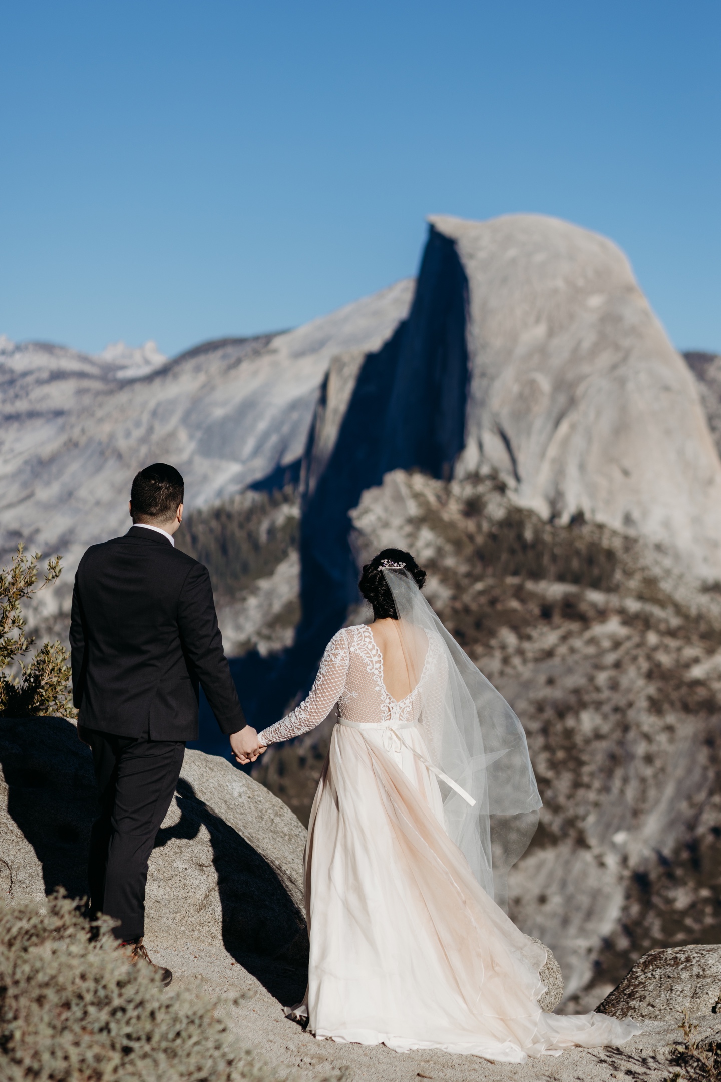 Bride and groom hold hands as they look out at Half Dome in Yosemite National Park.