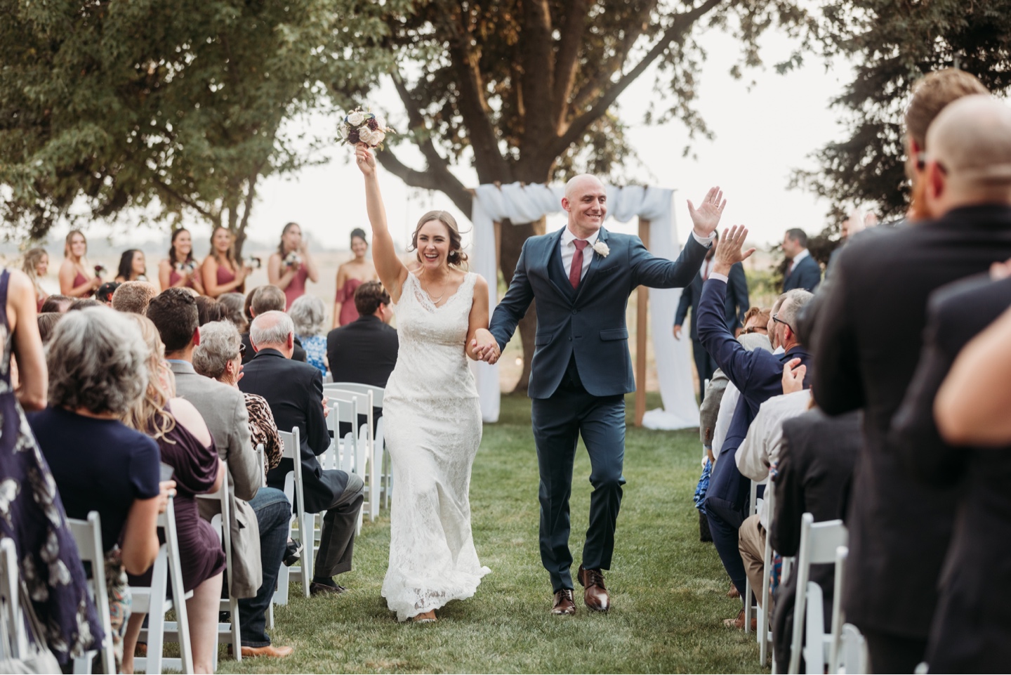 Newly married husband and wife walk down the aisle high fiving and cheering with their wedding guests. Wedding photography in Sacramento by Liz Koston.