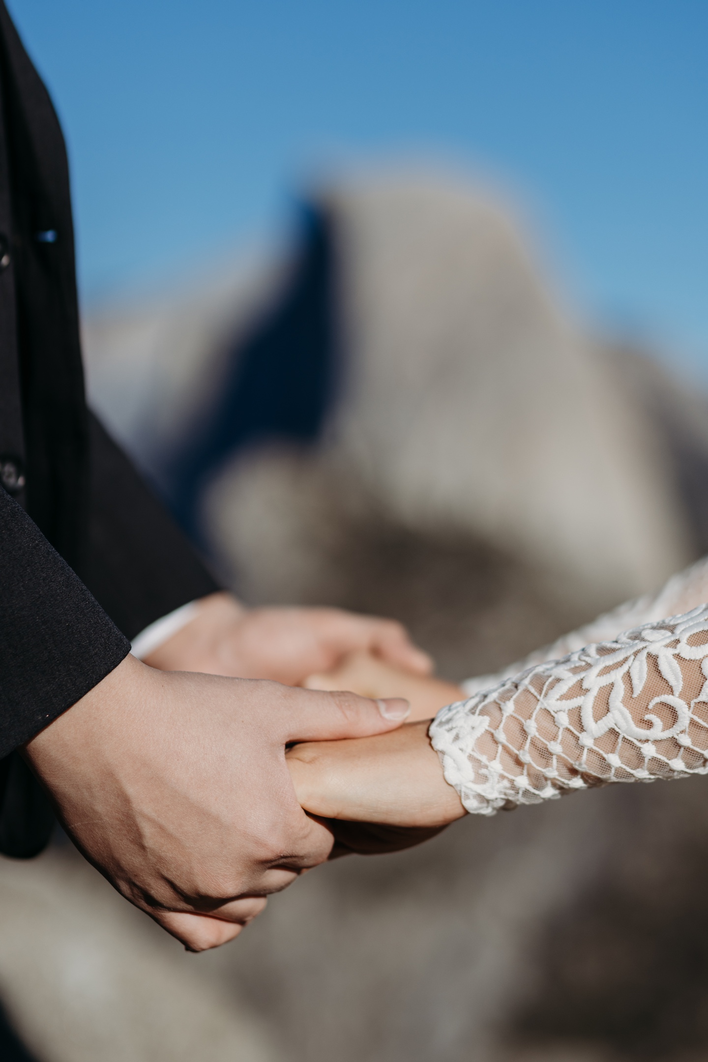 Close up of bride and groom holding hands with Half Dome in the distance after their Yosemite wedding.
