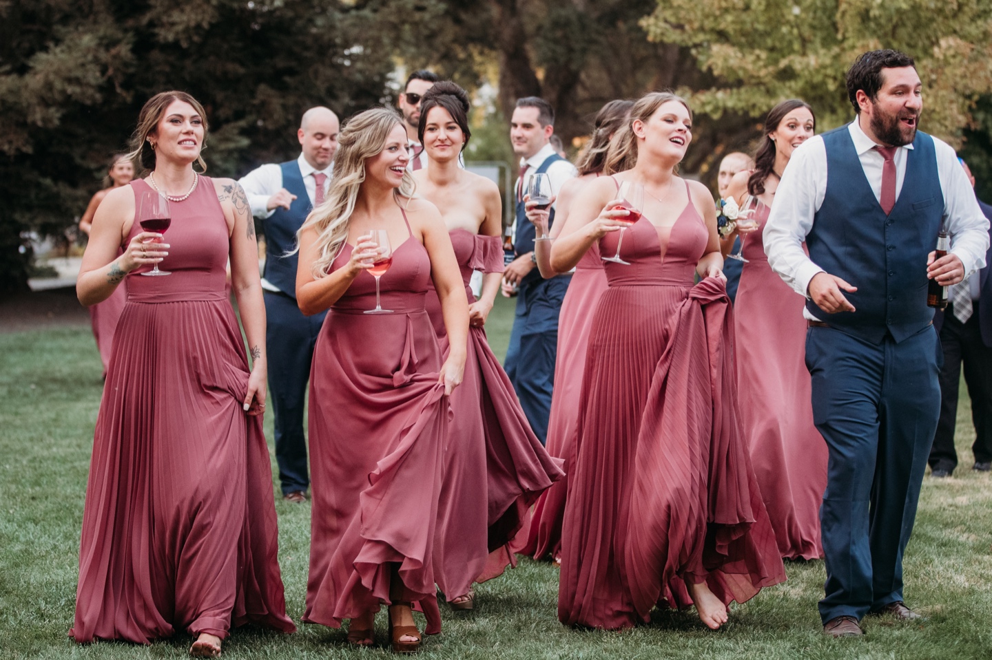 Bridal party walk into the wedding reception holding glasses of wine and beer.