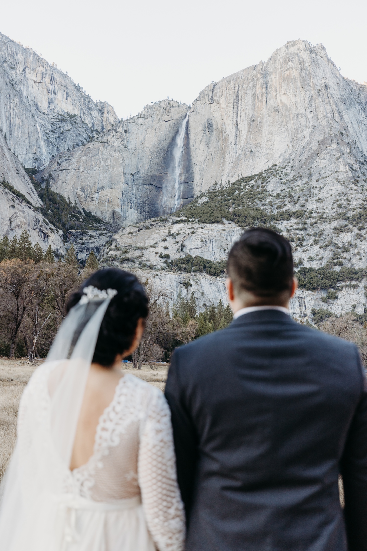 Bride and groom gaze a Yosemite Falls in their wedding attire.