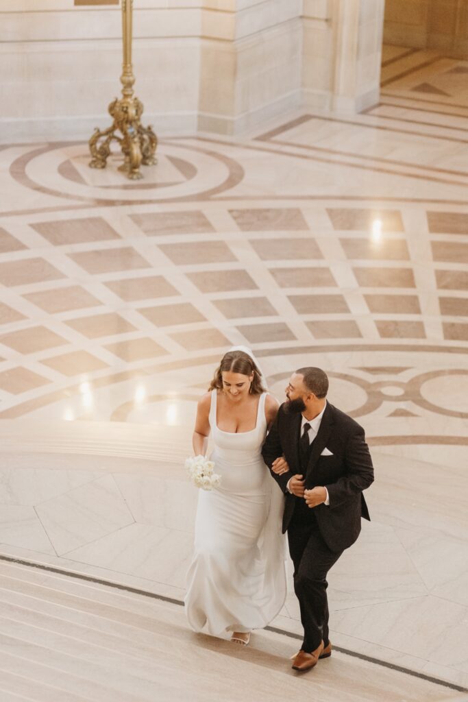 Bride and groom walk arm in arm up the Grand Staircase in San Francisco City Hall. Photo by Liz Koston Photography.