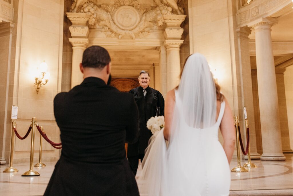 Bride and groom walk towards the officiant for their civil wedding ceremony at San Francisco City Hall. Photo by Liz Koston Photography.