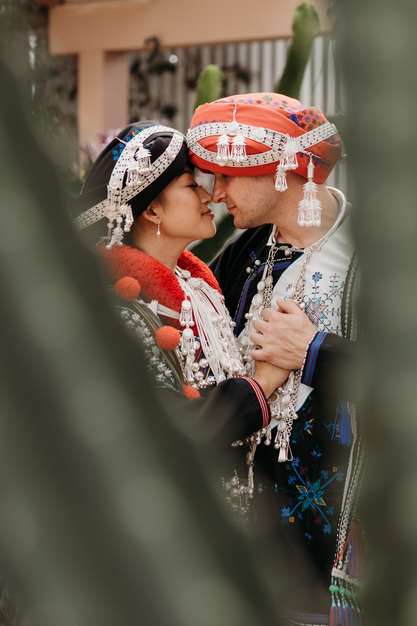 Bride and groom embracing while wearing their Mian wedding attire as seen through green leaves at the Prickly Pear. 