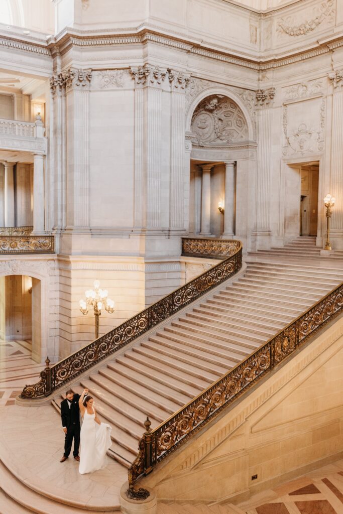 Groom spins bride and the bottom of San Francisco City Hall's Grand Staircase during their City Hall wedding. Photo by Liz Koston Photography.
