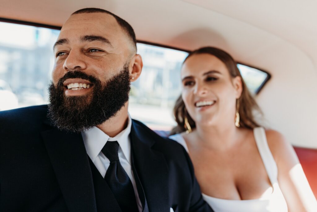 Bride and groom smile in the back of a car. Photo by Liz Koston Photography.