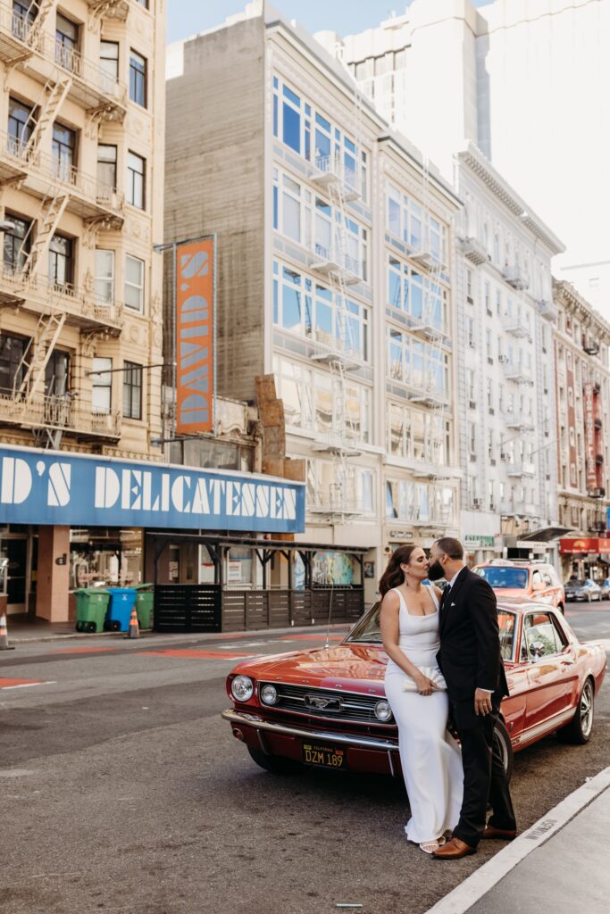 Bride and groom kiss in front of a red vintage Mustang in San Francisco, California. Photo by Liz Koston Photography.