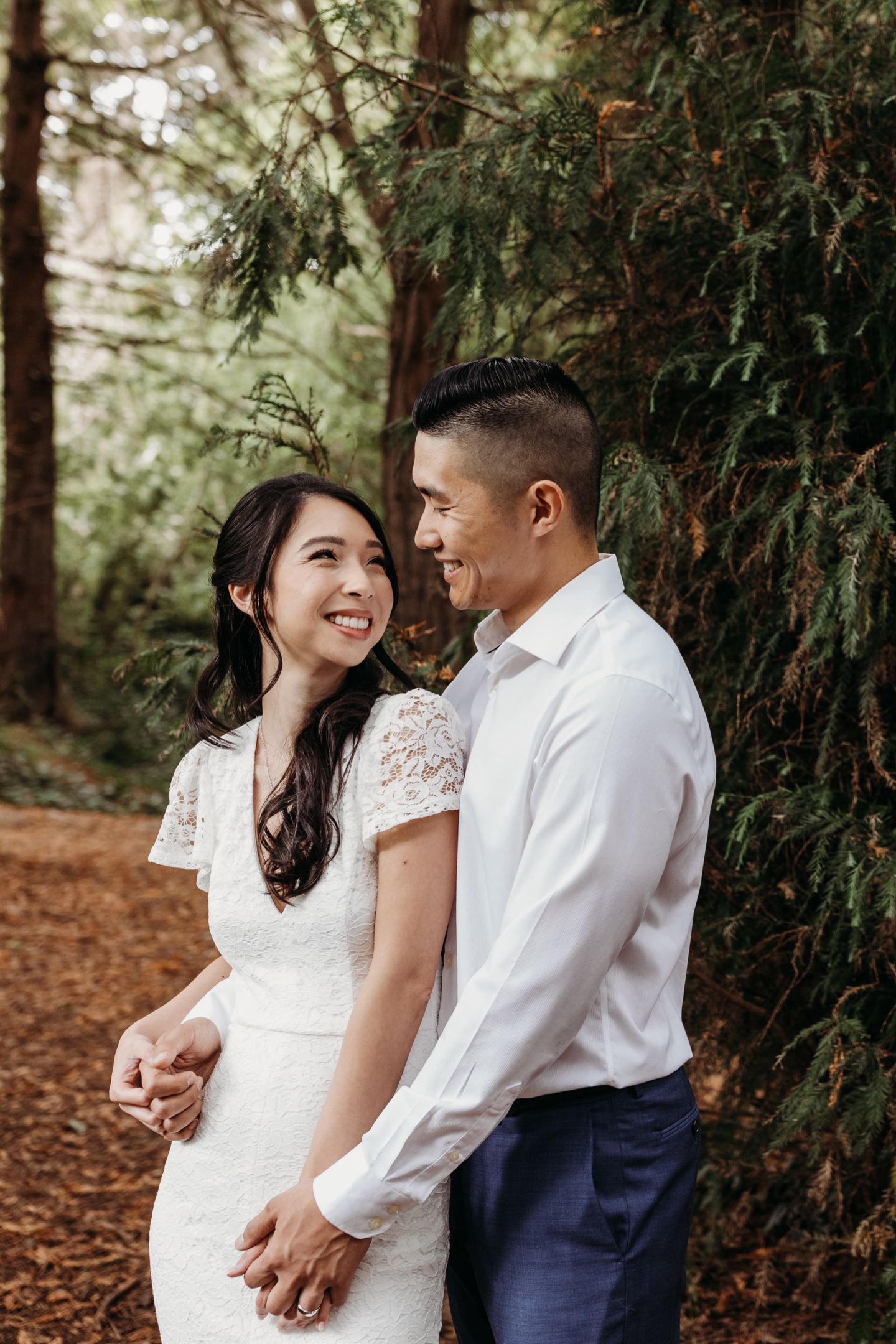 Bride and groom stand embracing in Golden Gate Park while smiling at each other after their San Francisco City Hall elopement.