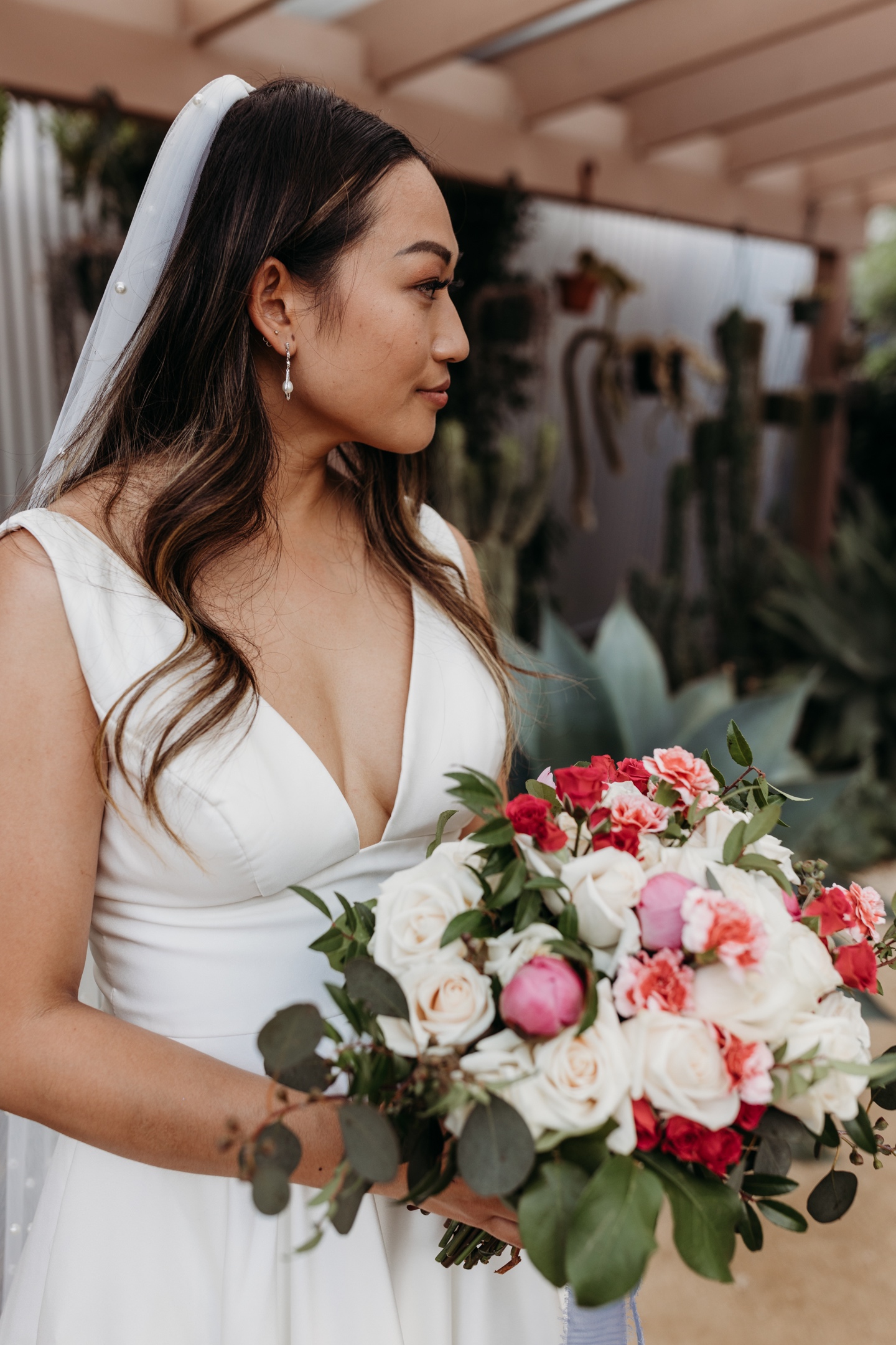 Profile of the bride in her wedding dress holding her bouquet of red, white, and pink flowers. Liz Koston Photography.